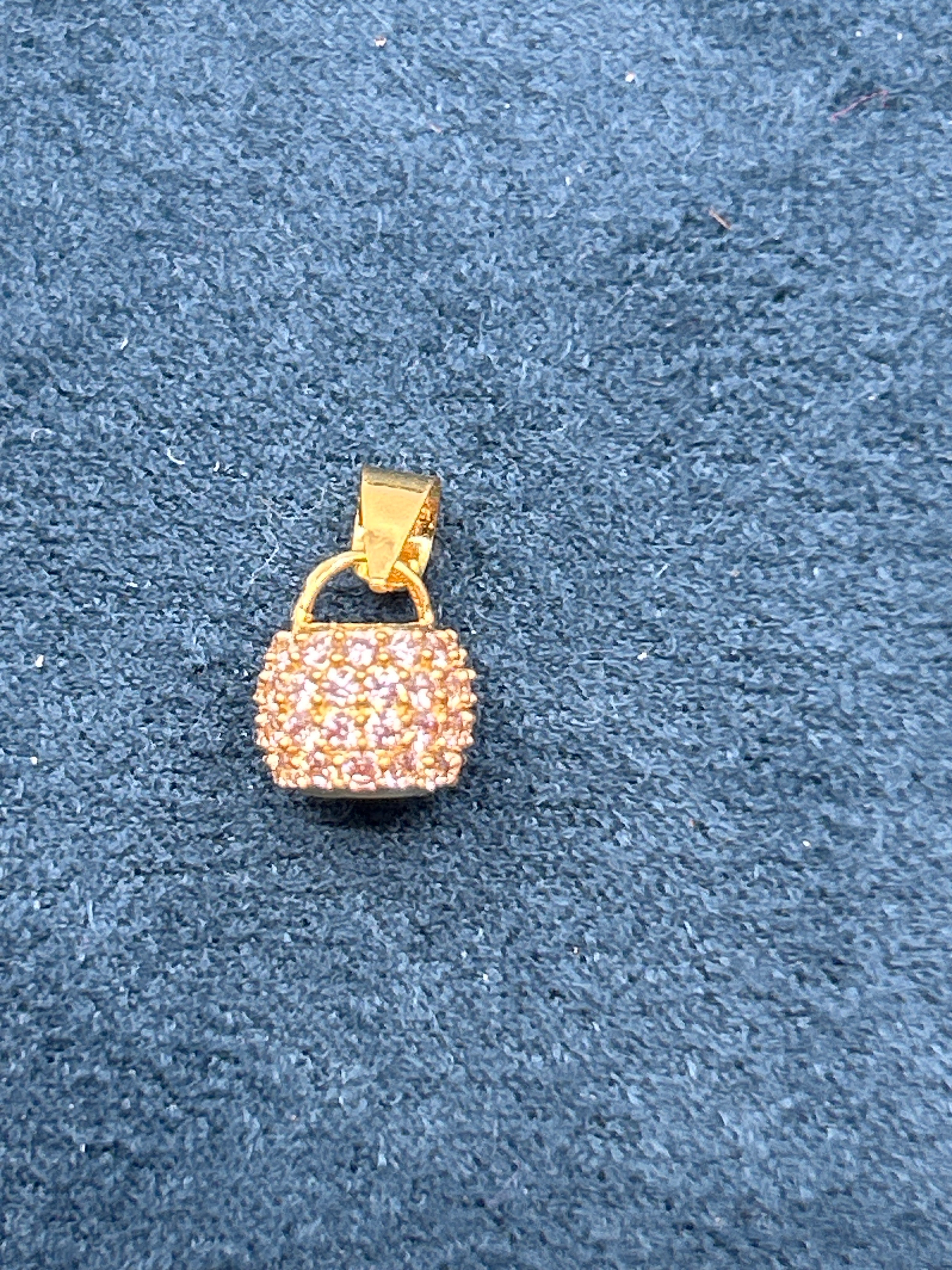 Gold mug-shaped pendant with gemstones on a gray background