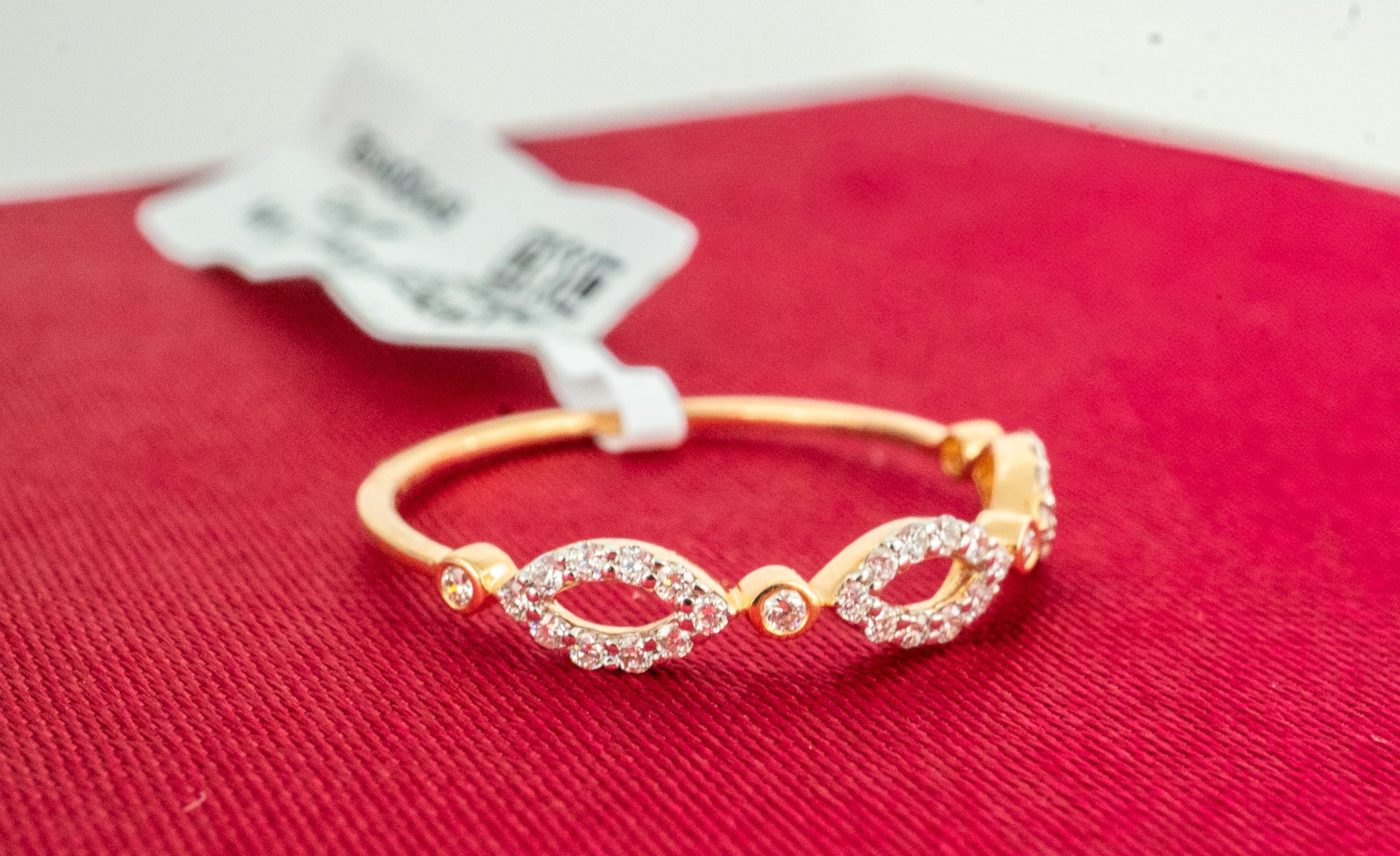 18k gold diamond infinity band ring with pavé-style geometric links, photographed on red fabric background.
