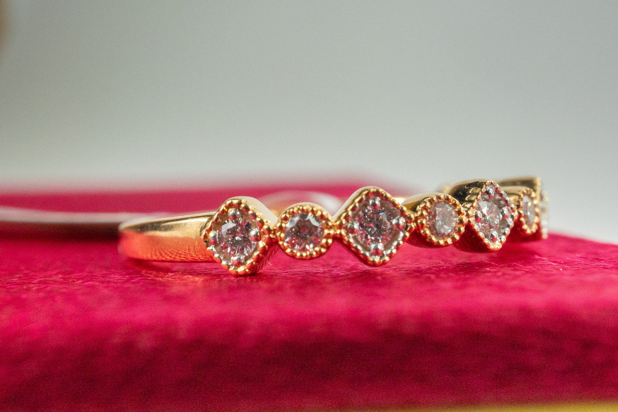 18k gold diamond station band ring photographed on a red surface showing the alternating round and square diamond stations
