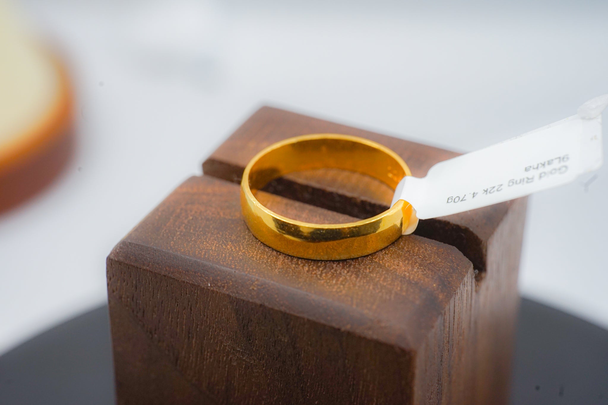 22K gold band ring (4.70g) displayed on a wooden stand with a paper tag.
