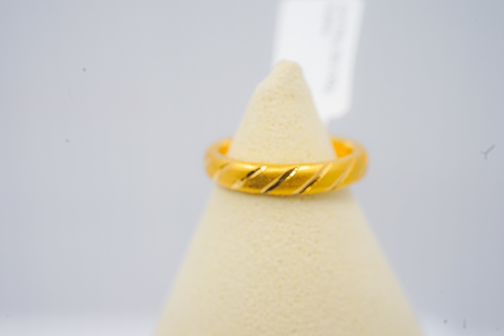 22K yellow gold band ring with diagonal groove design, displayed on a light jewelry stand