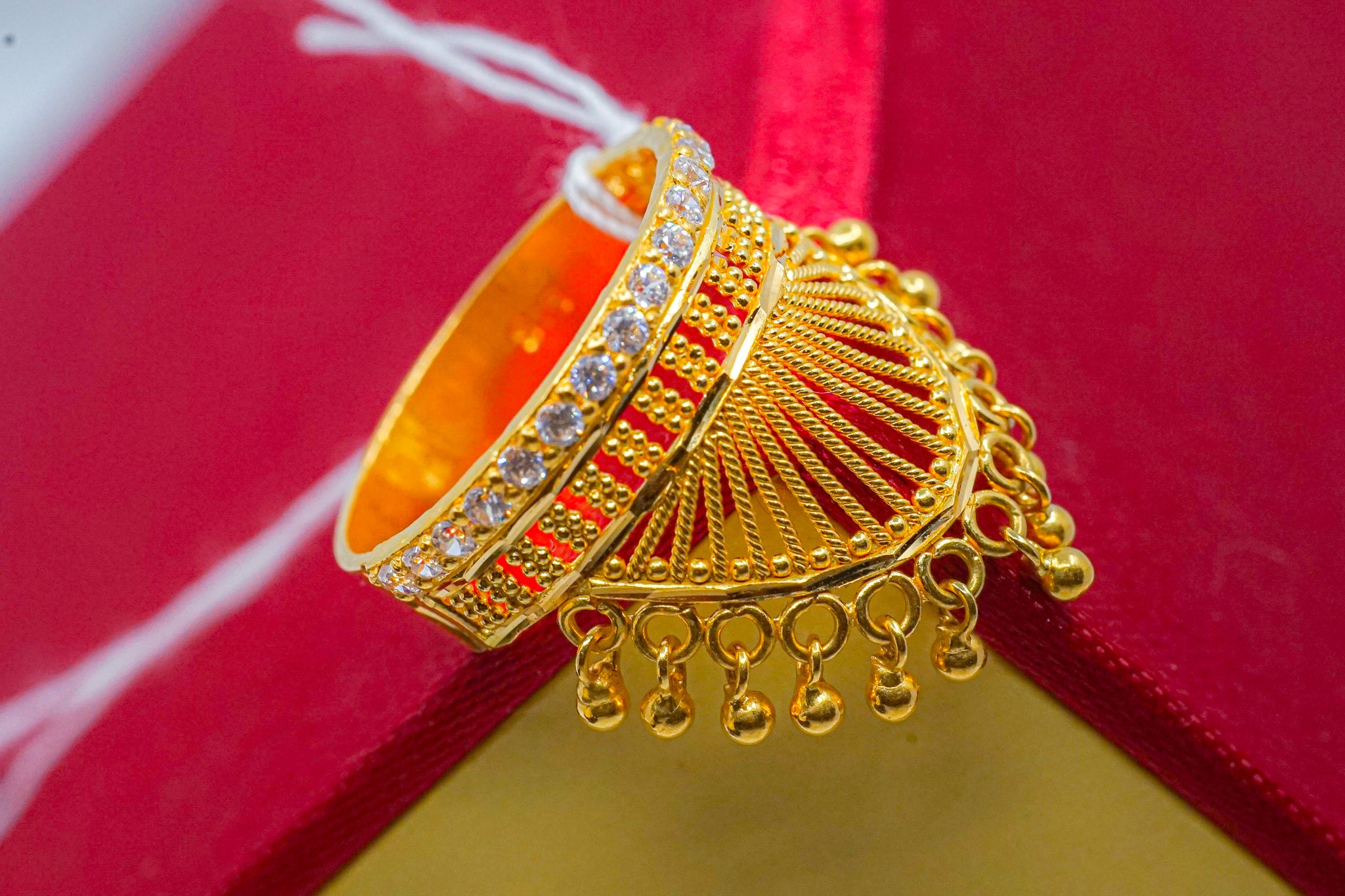 22K yellow gold ring with fan-shaped top, clear stone accents, and dangling drop details on a red and yellow box
