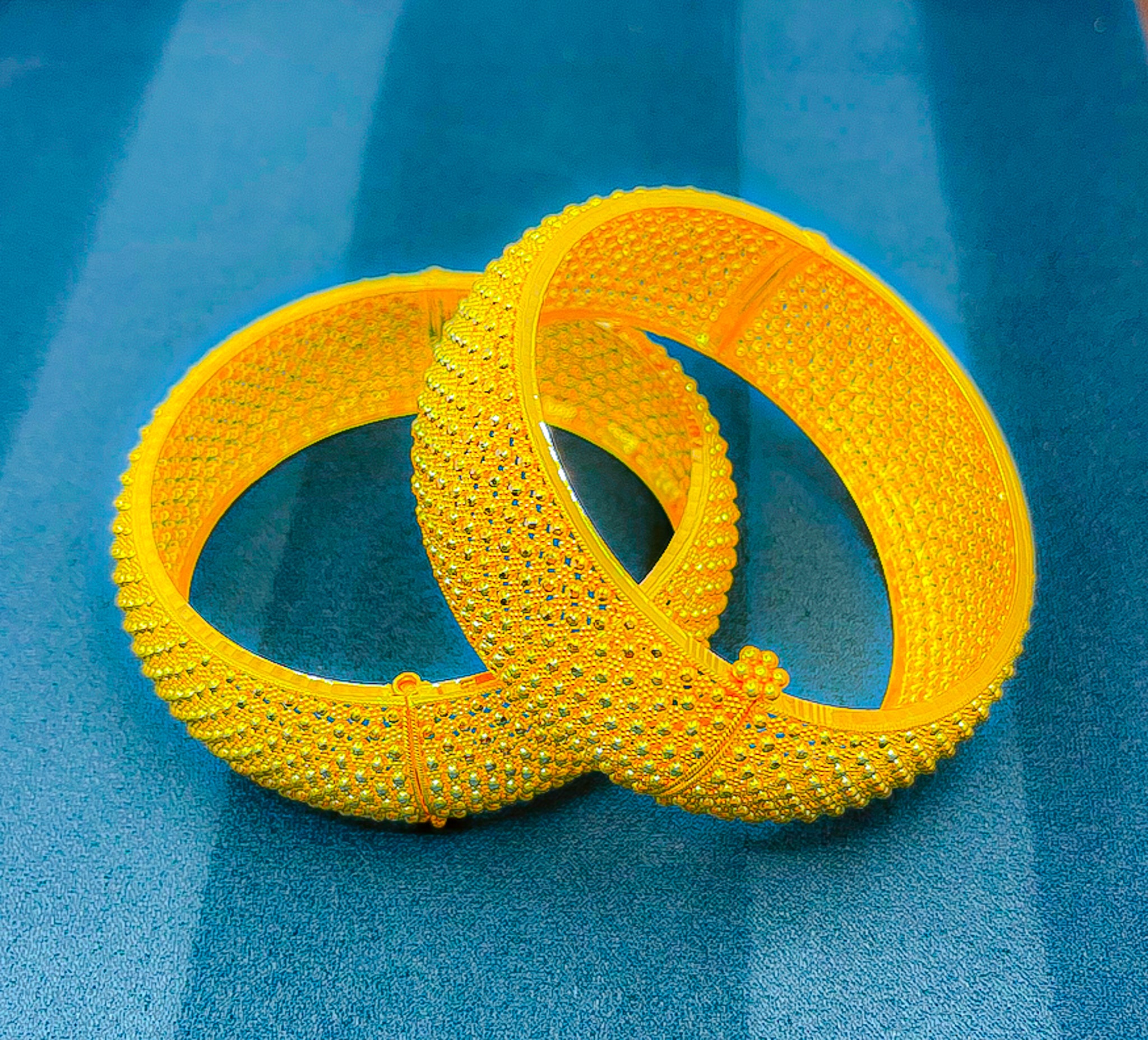 22K yellow gold wide textured bangle set (2 pcs) on blue jewelry tray