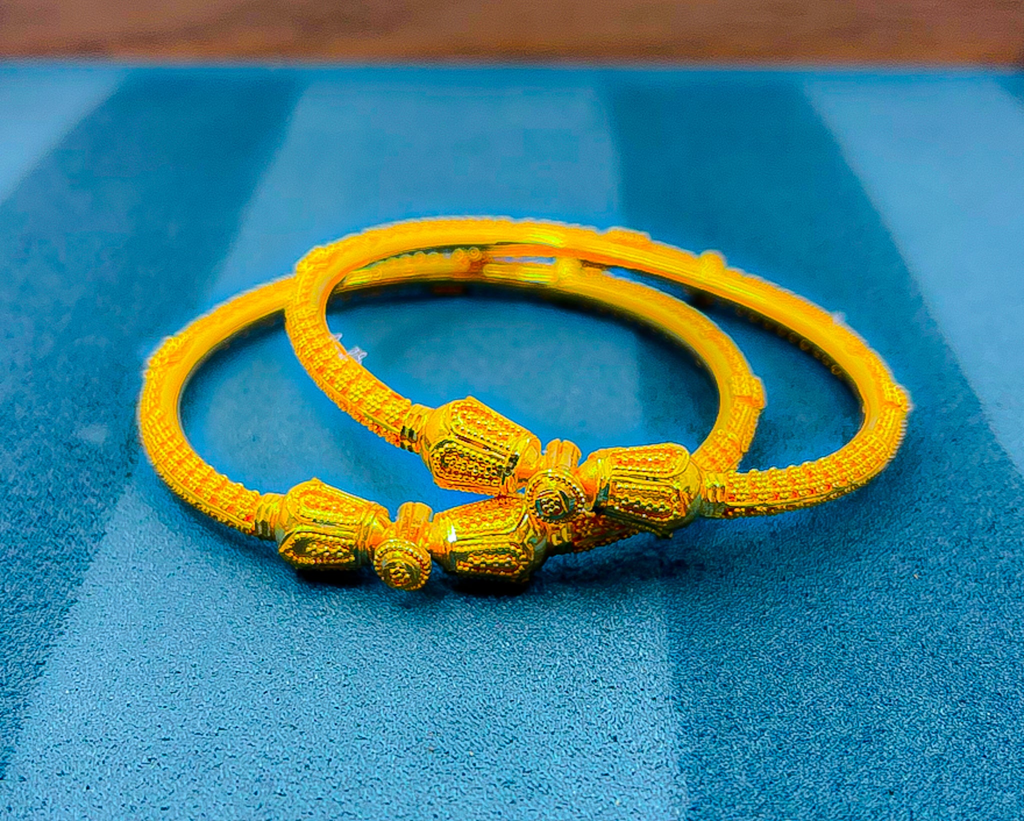 22K yellow gold bangle set (2 pieces) with textured pattern on blue background