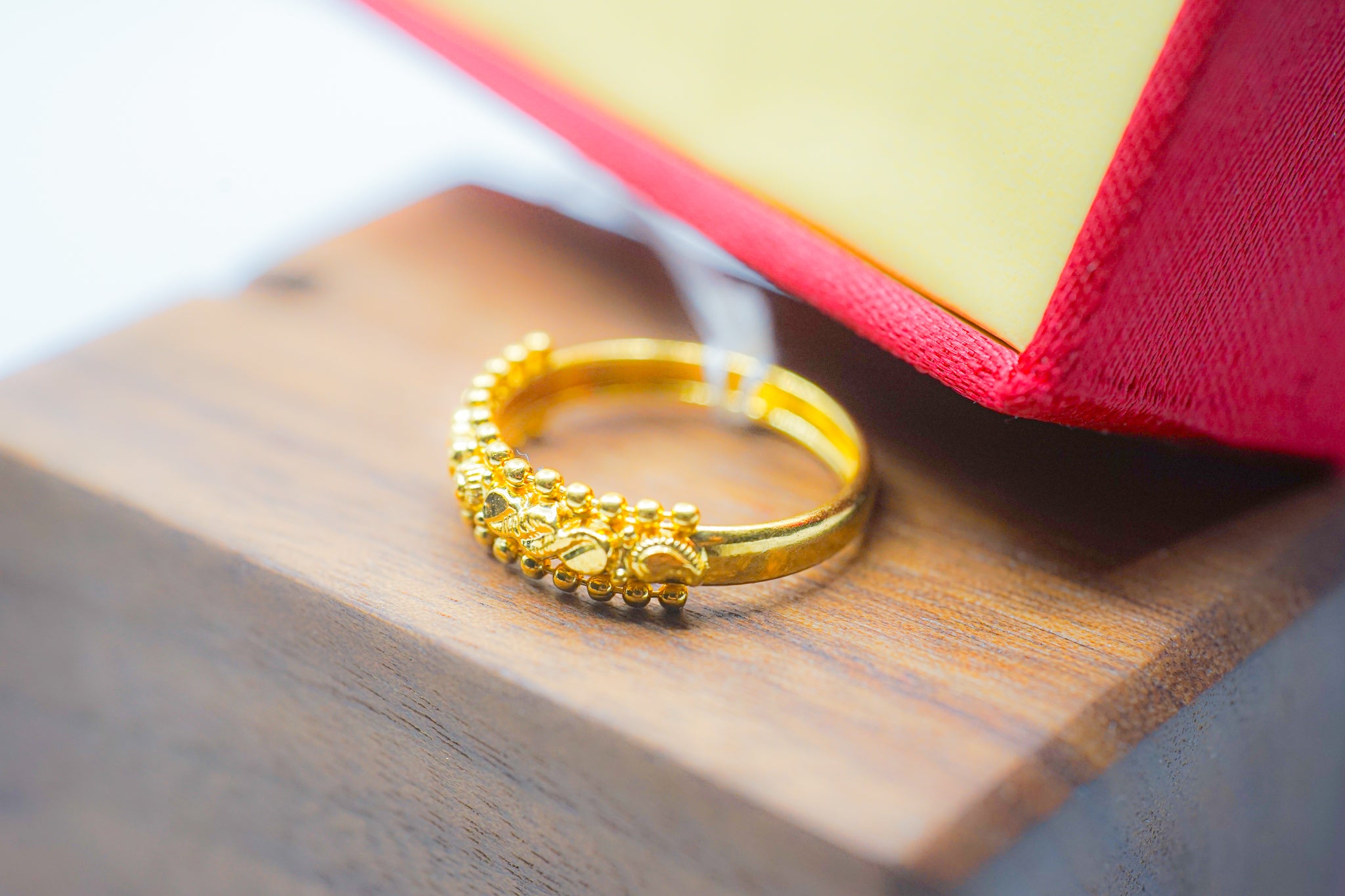 22k gold beaded band ring on a wooden display with a red jewelry box in the background