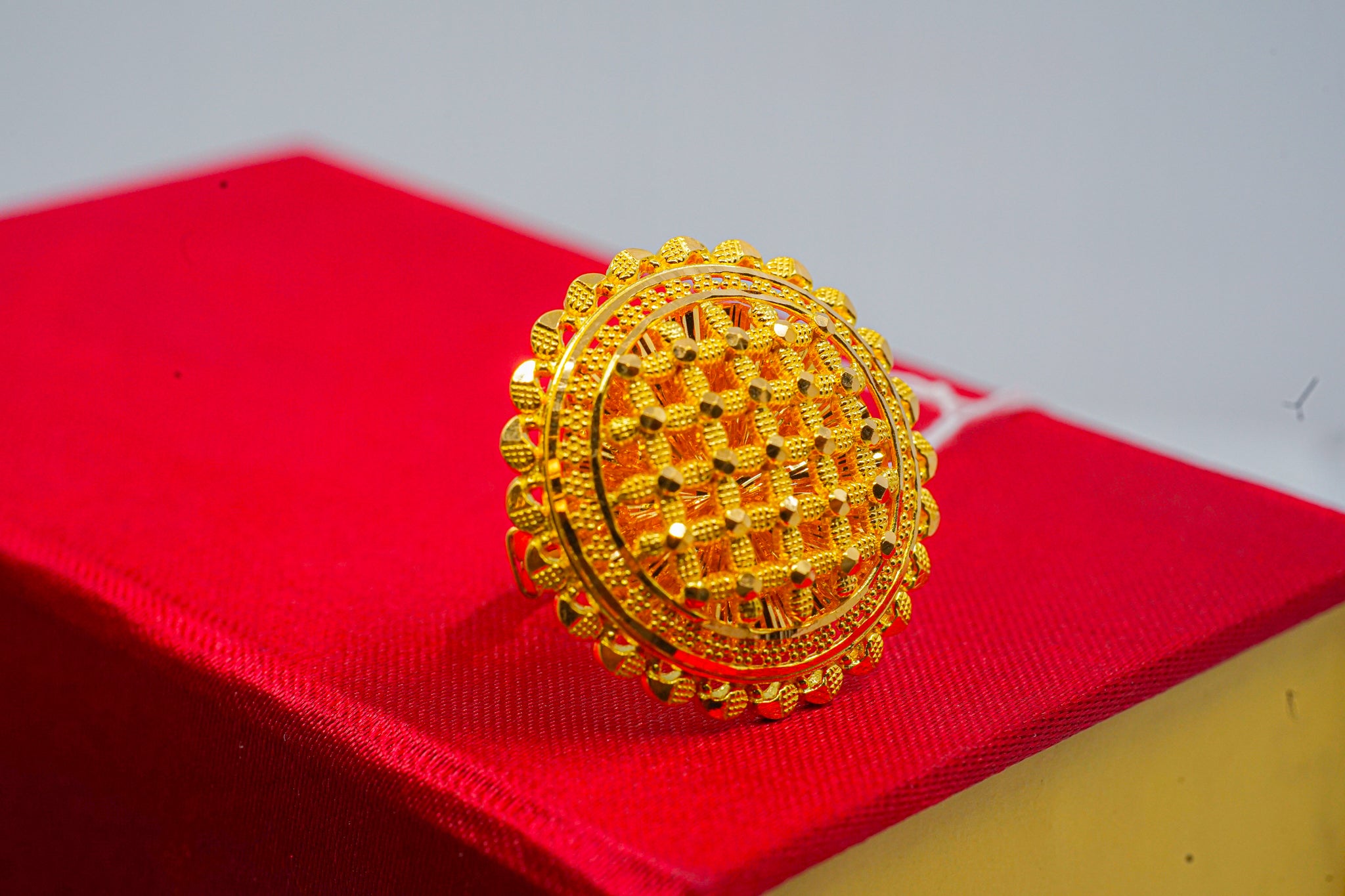 22k gold statement ring with round beaded face and textured lattice pattern, shown on a red jewelry box.