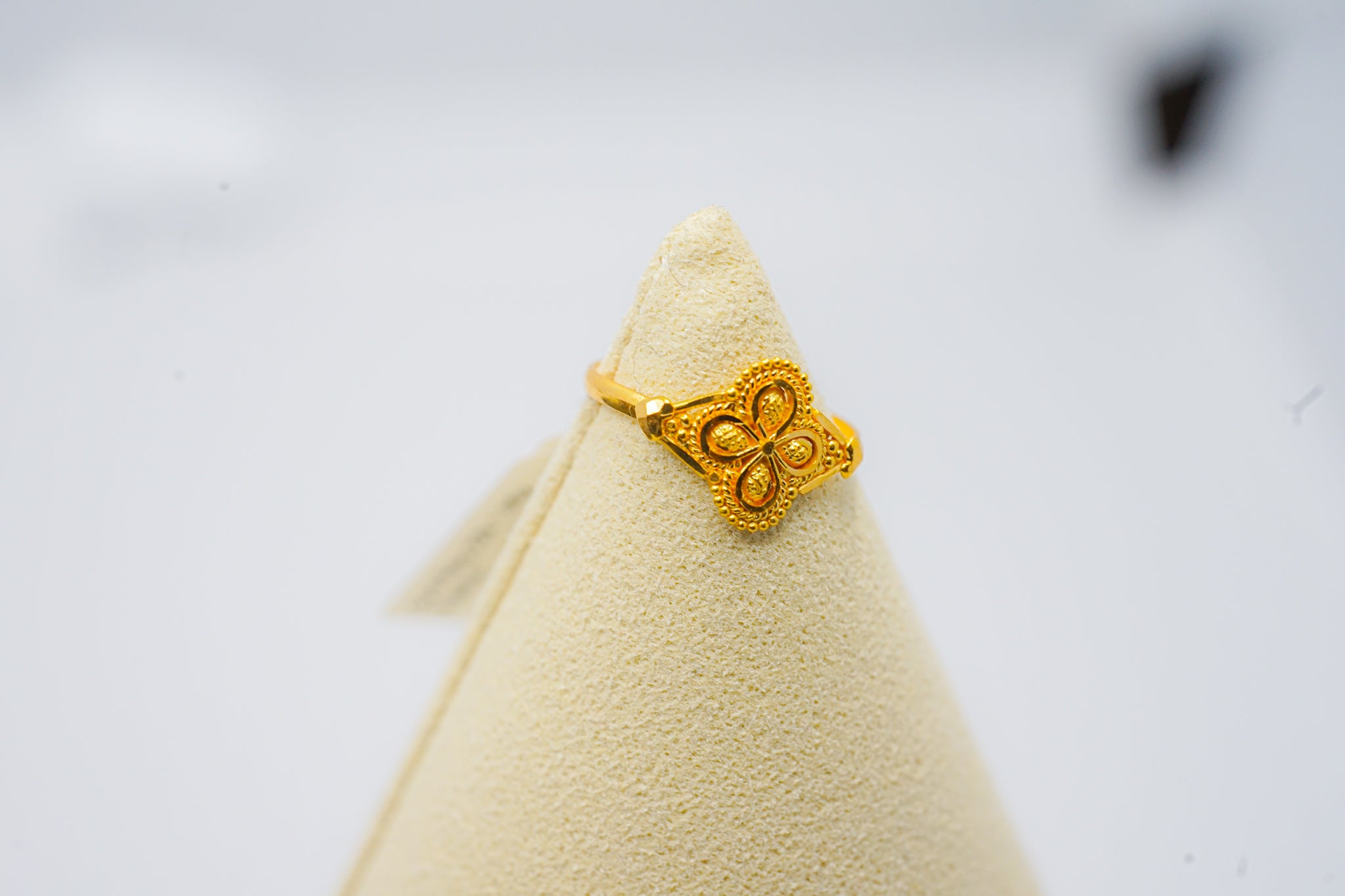 22k gold ring with square top and clover motif, shown on a cone stand against a white background.