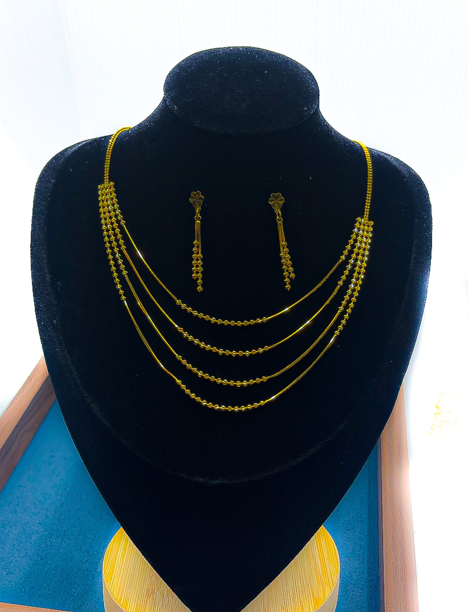 22k gold layered necklace with matching drop earrings on a black velvet display bust