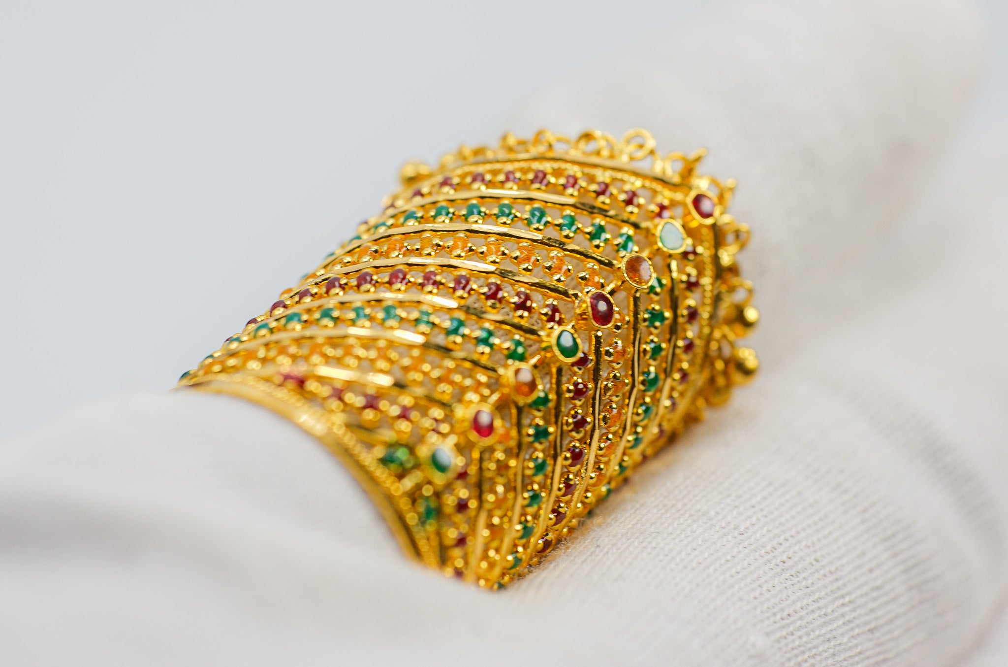 Angled view of a 22K gold wide statement ring with red and green stones and dangling bead fringe, size 9.5.