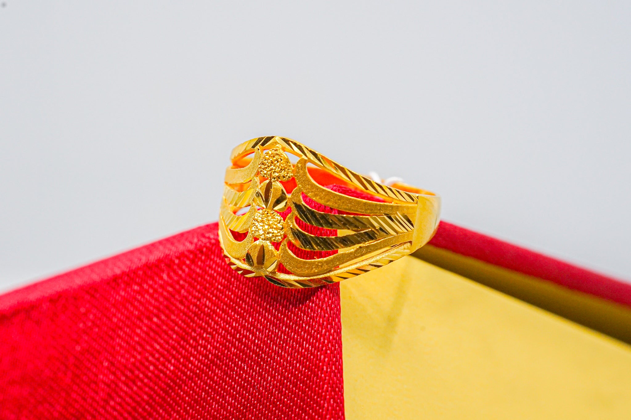22k gold wide band ring with geometric cutout design on a red and yellow jewelry box