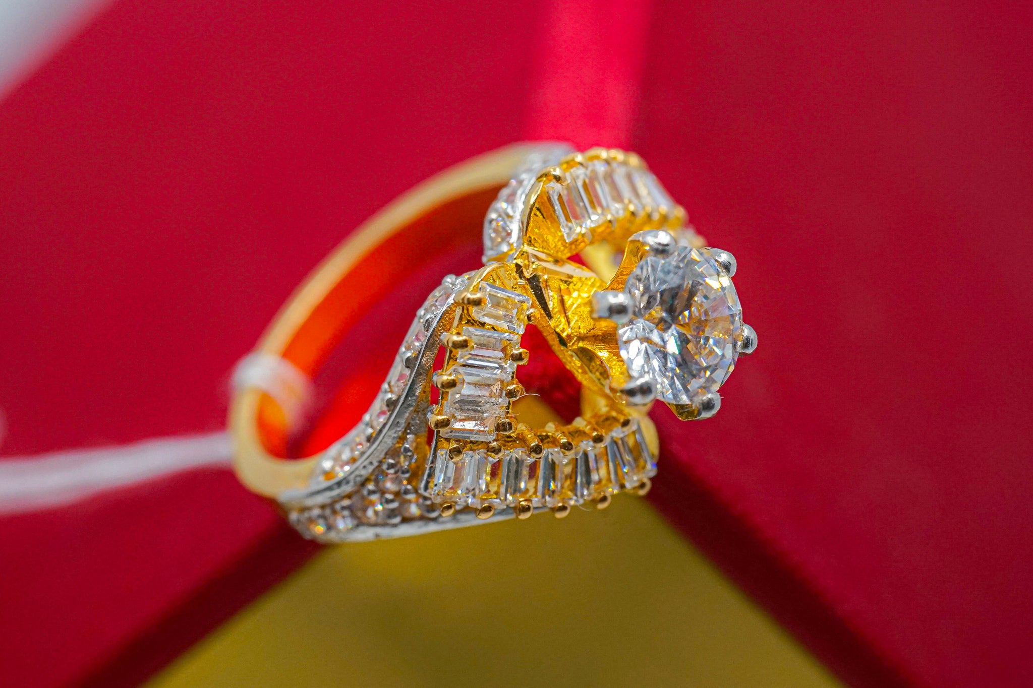 22k gold ring with clear round center stone and baguette-style accent stones on a red and yellow background