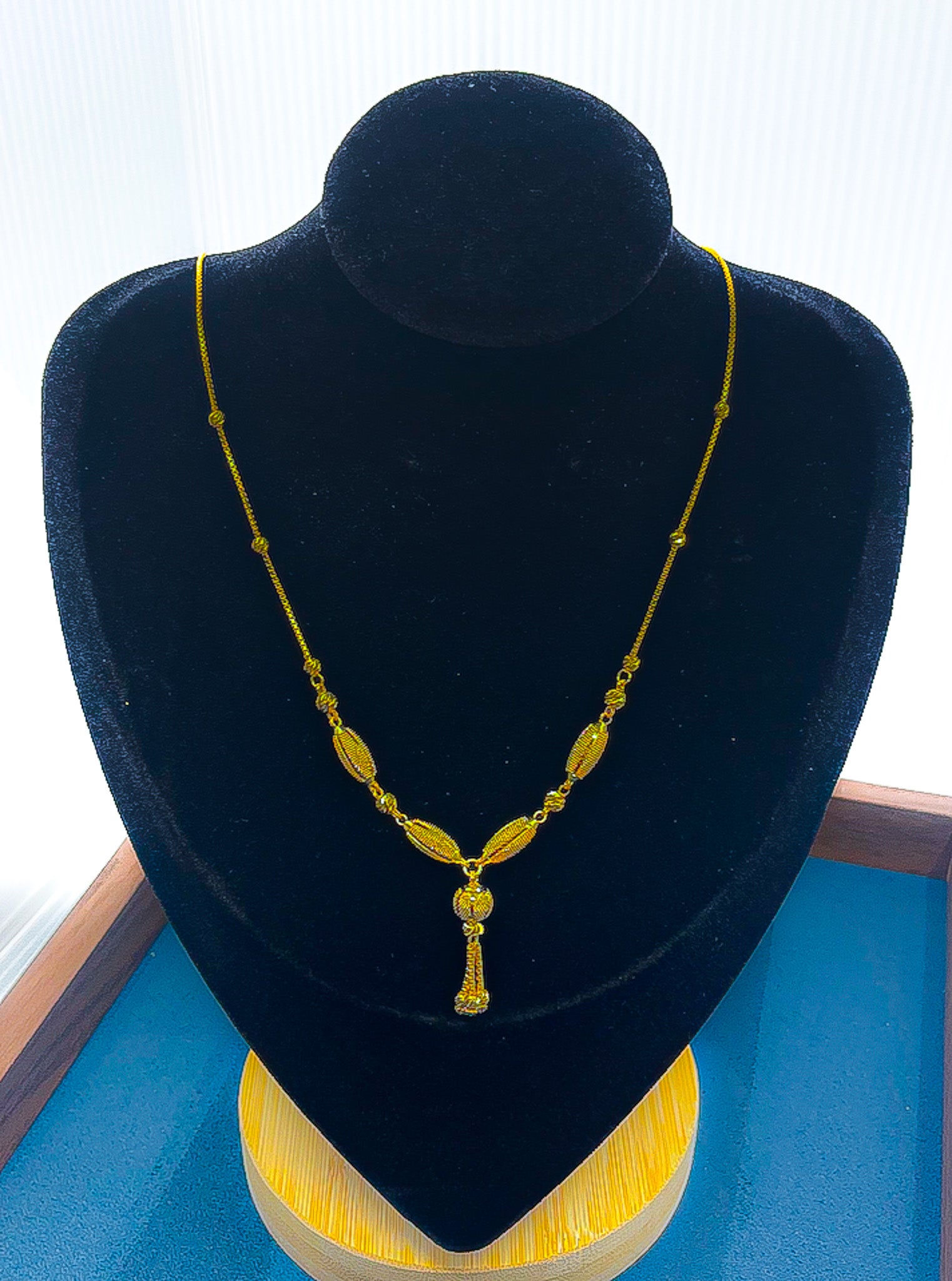 22k gold station necklace with center drop pendant on black velvet display bust