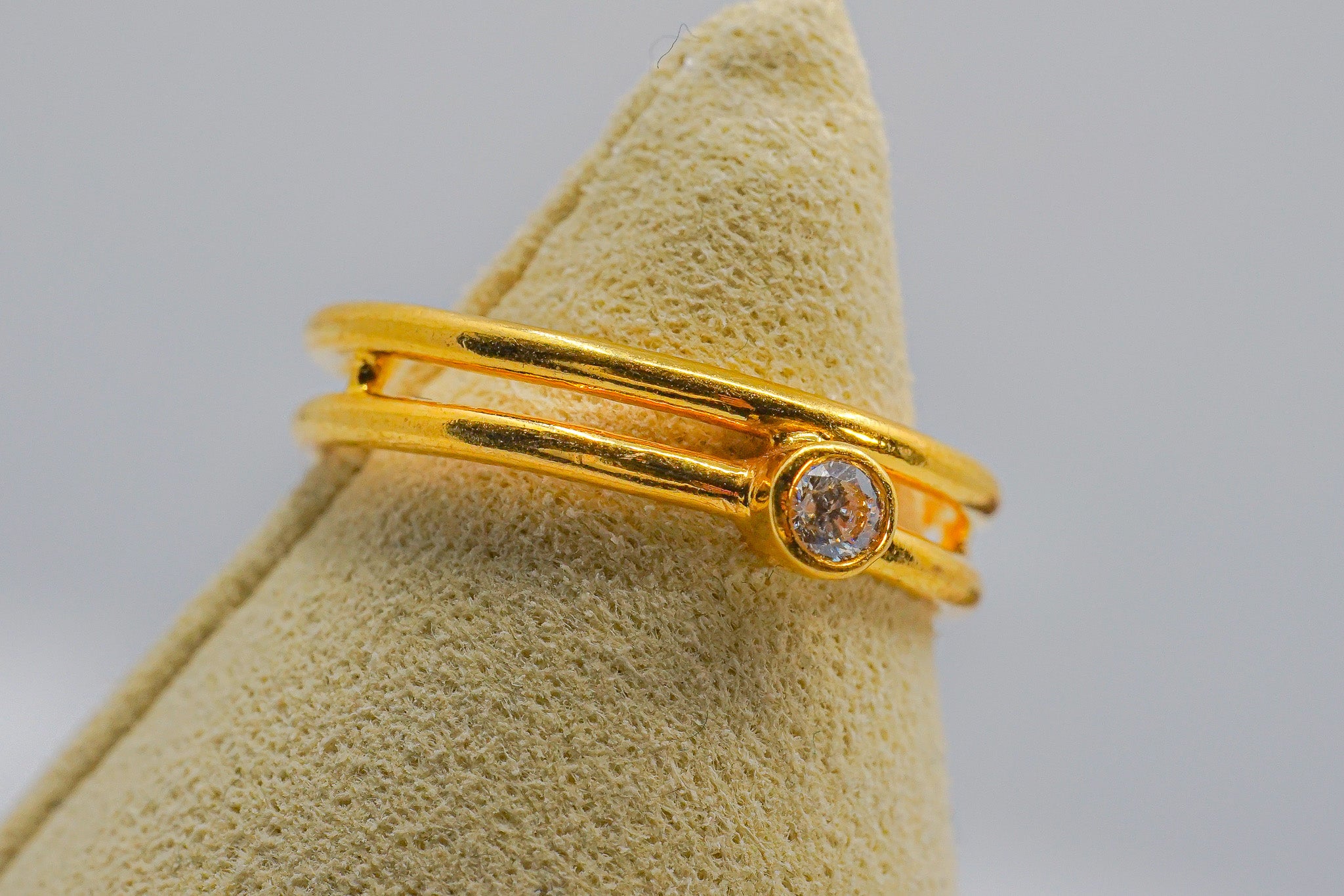 Side view of 22K gold ring showing bezel-set clear round zirconia and stacked triple bands