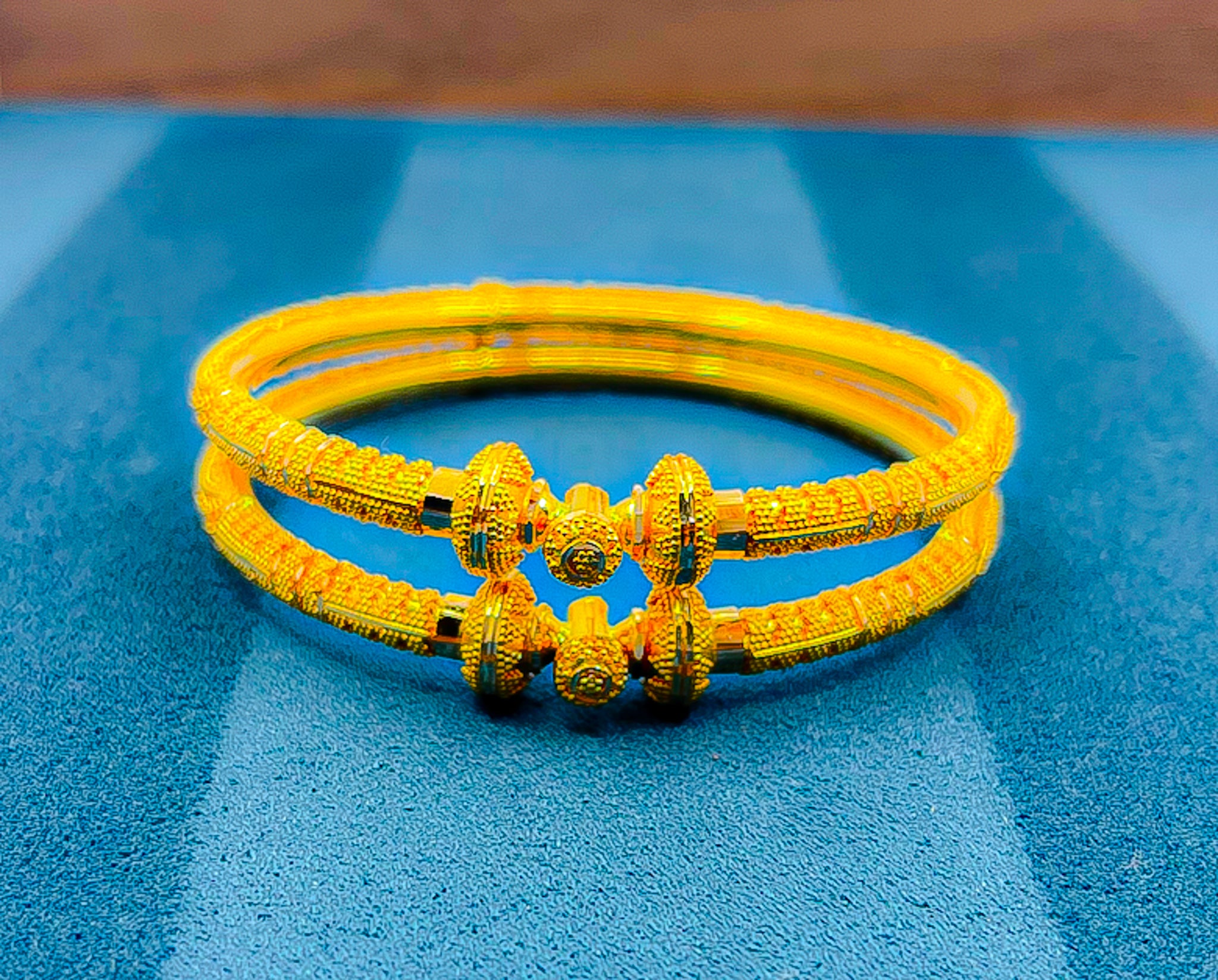 Close-up of 22K yellow gold textured bangle set with decorative end detail held on white glove