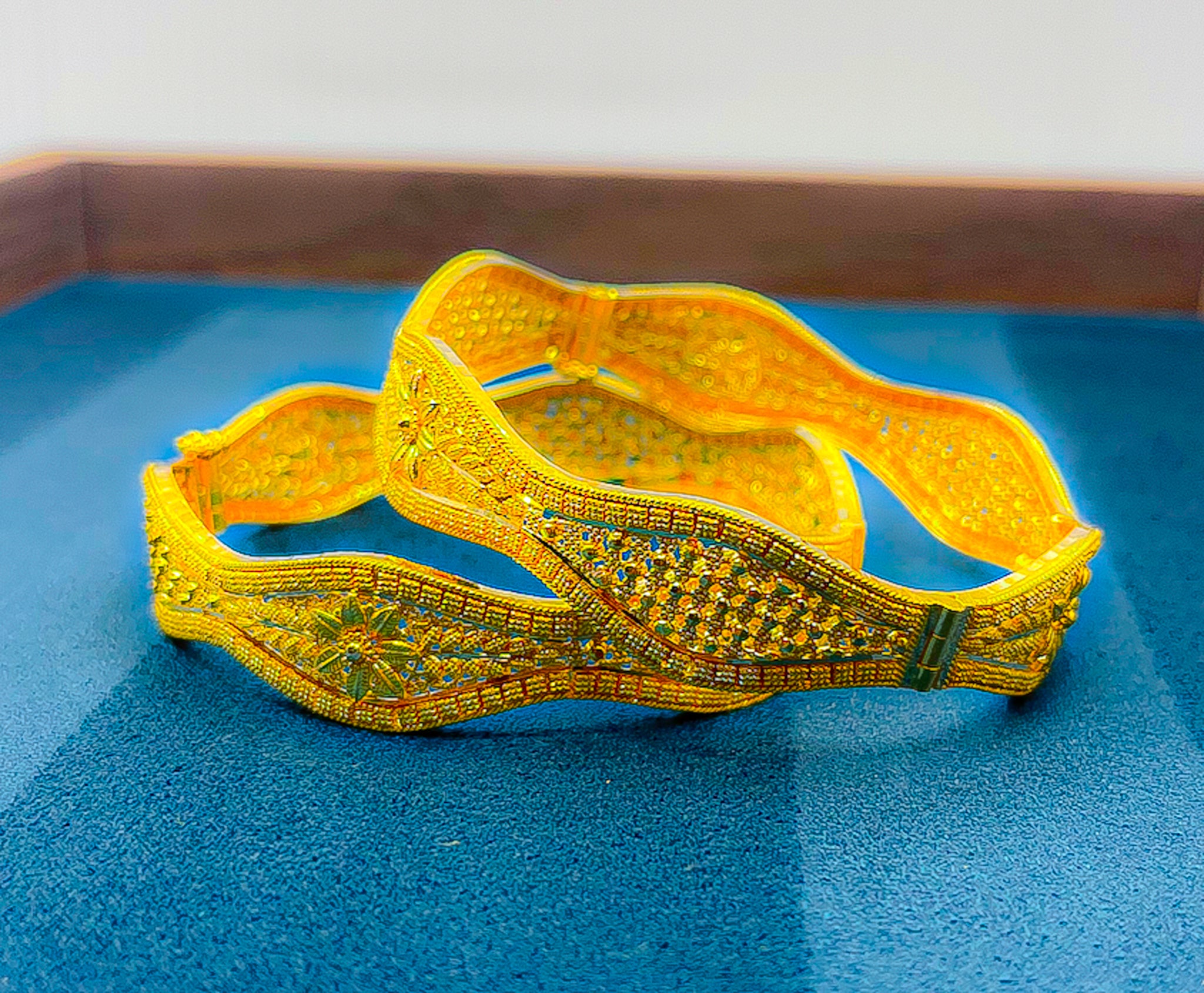 Two 22k yellow gold wide bangles (2-piece set) with detailed patterned design on a blue background