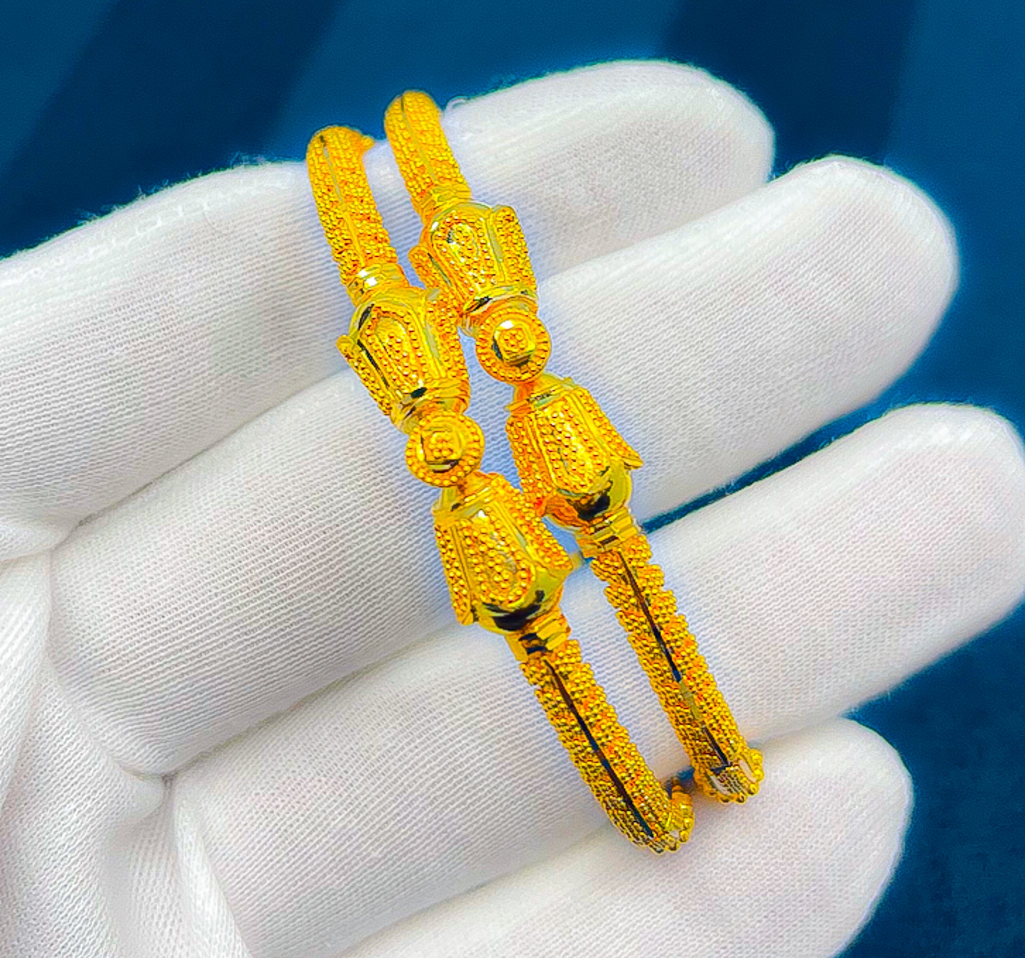 Close-up of two 22K yellow gold bangles showing decorative center design