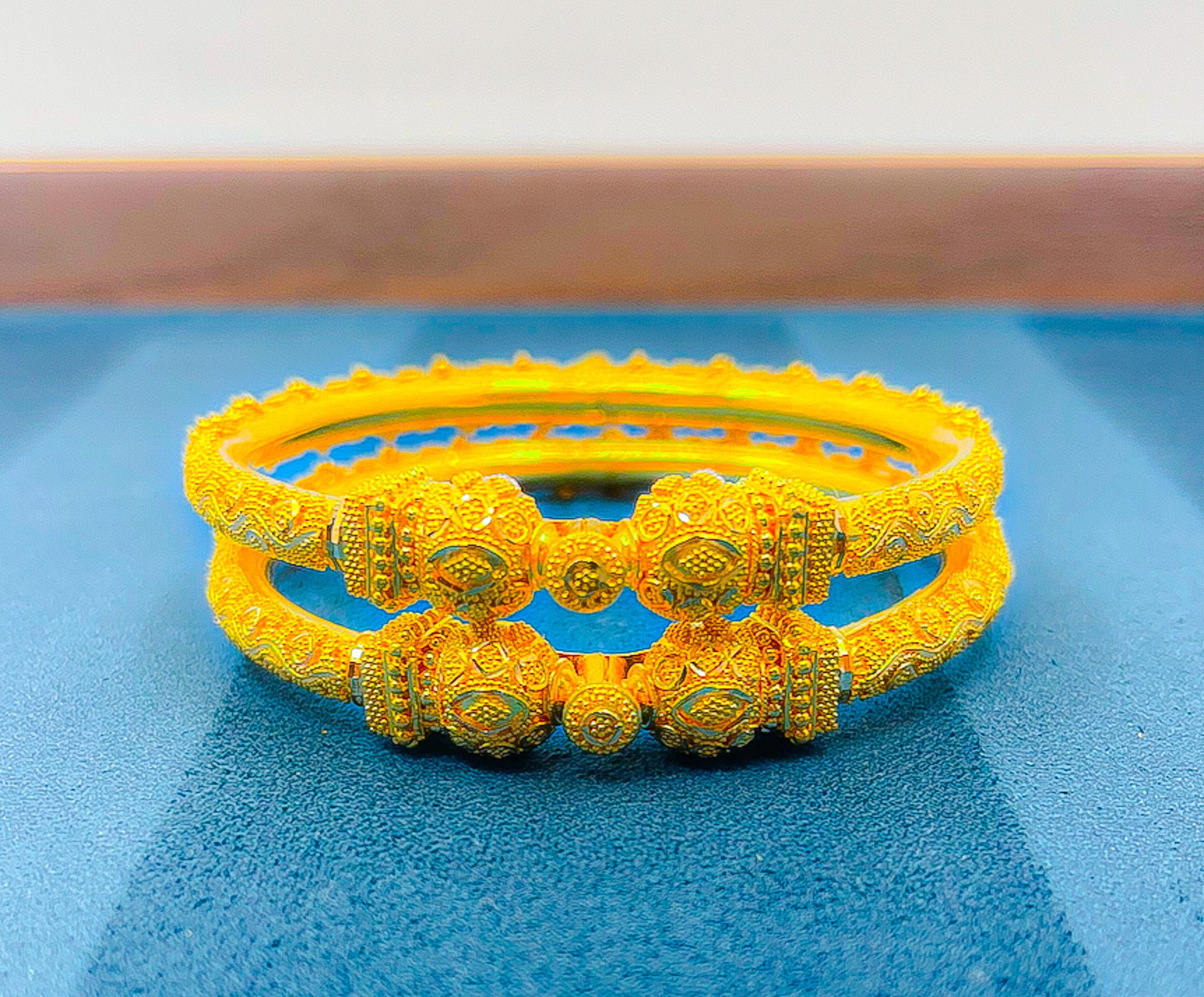Close-up of 22K yellow gold bangle set held on a white glove showing detailed pattern