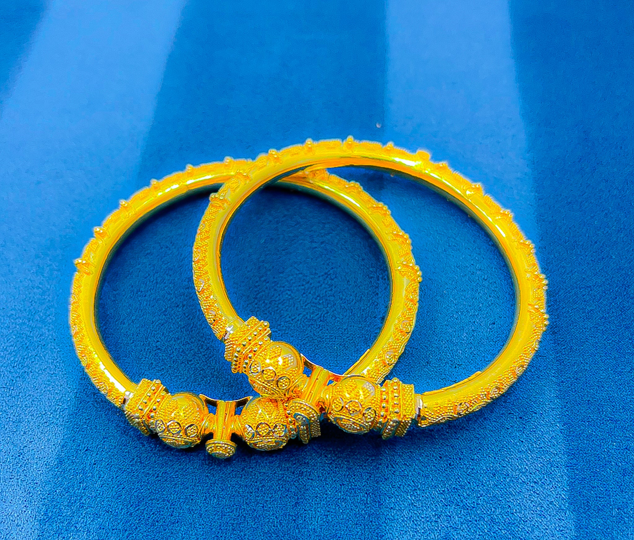 22K yellow gold bangle set held on a white glove