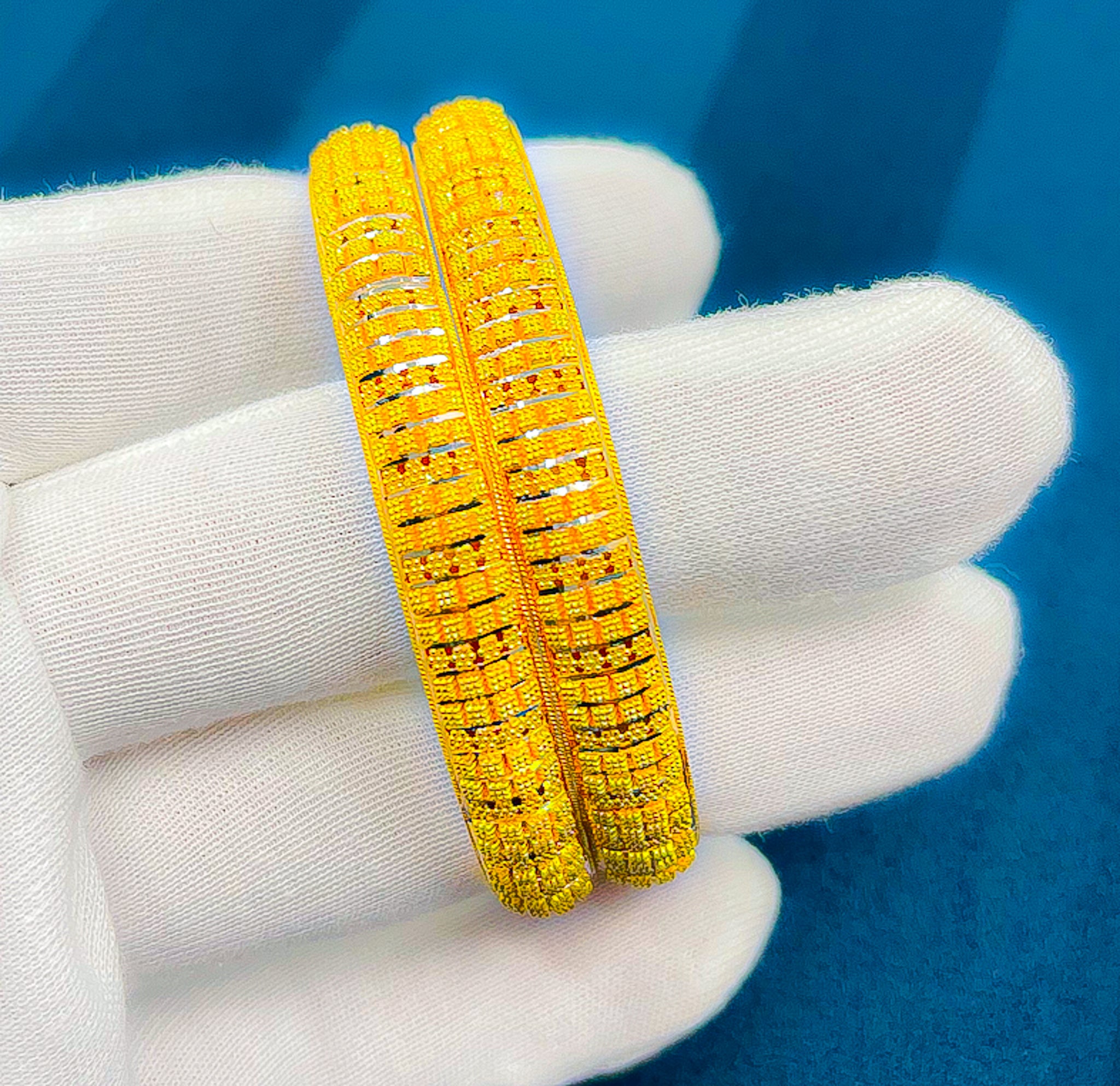 Close-up of 2PCS 22k yellow gold bangles with textured pattern held in a white glove