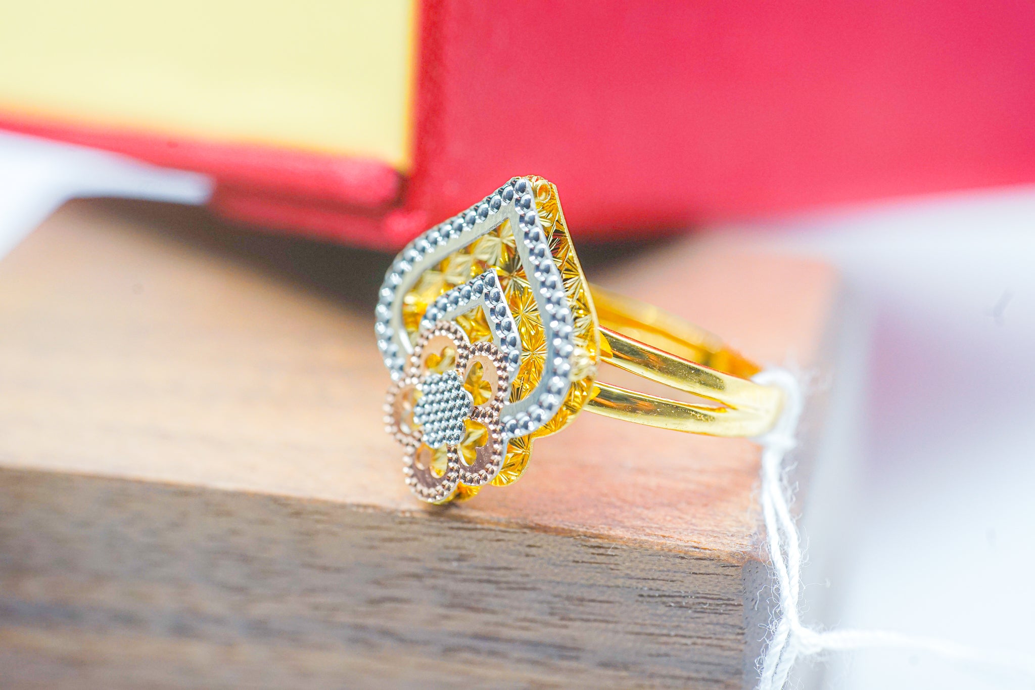 22k gold floral teardrop ring with three tone design on a wooden display and red jewelry box background