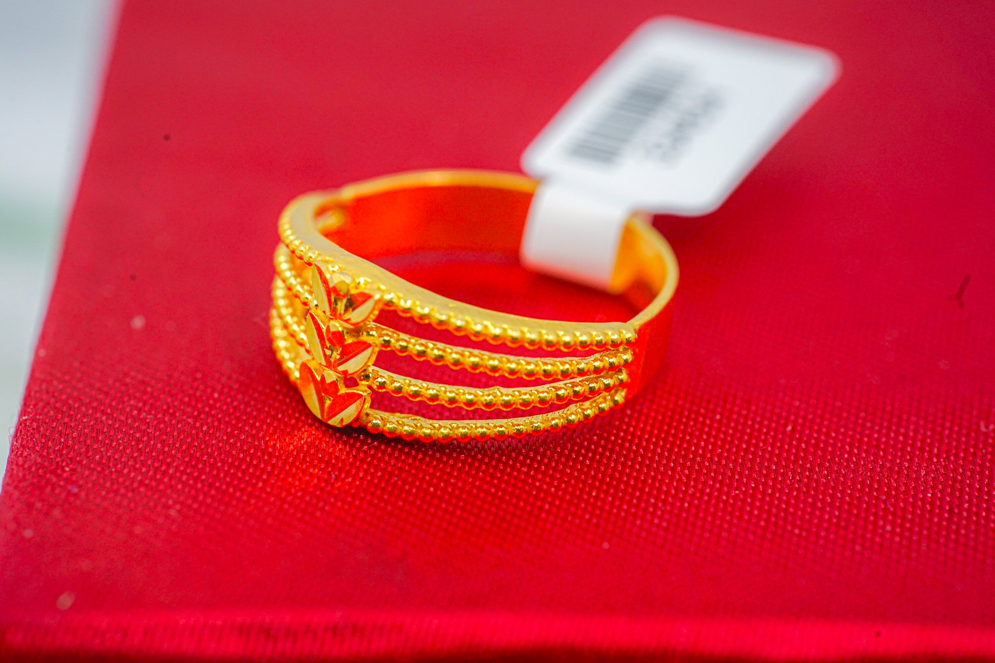 22k gold beaded band ring with triple-row texture and leaf motif on red background