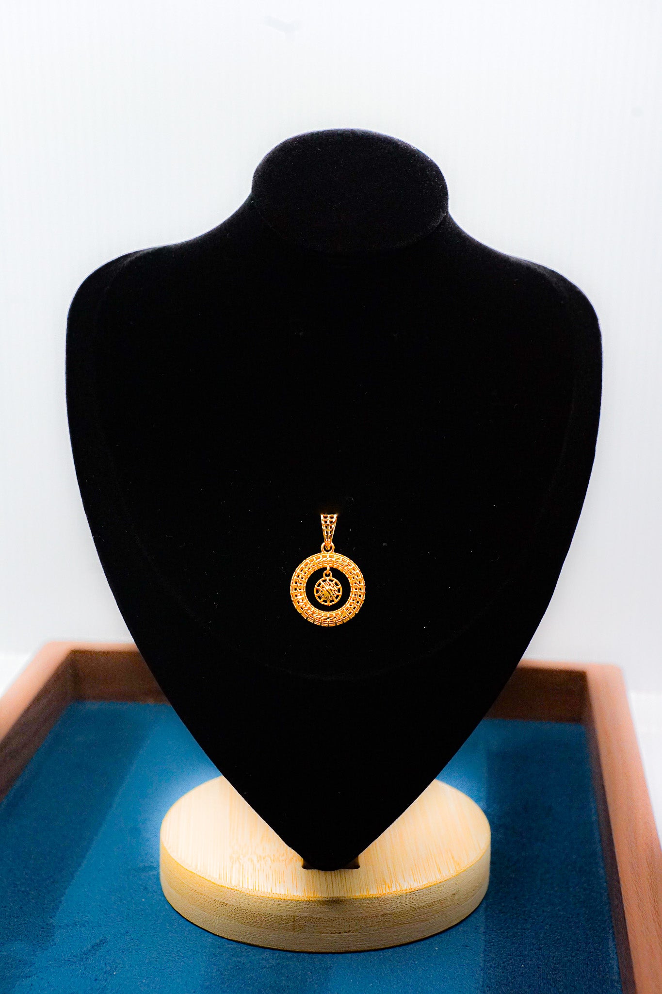 22k gold circle pendant with cutout center design on a black jewelry display bust.