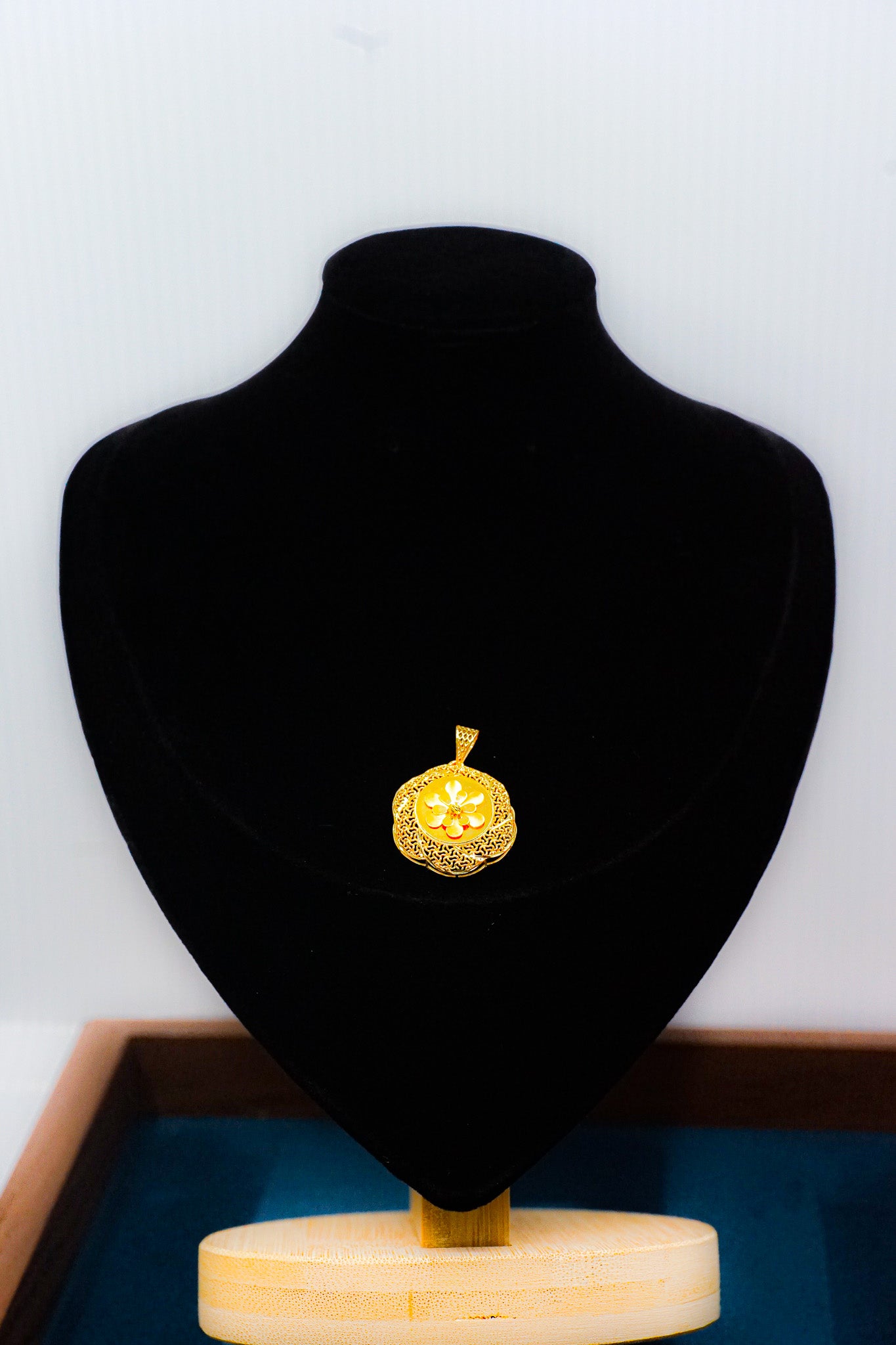 22k gold floral coin pendant with round disc design on a black jewelry display bust.