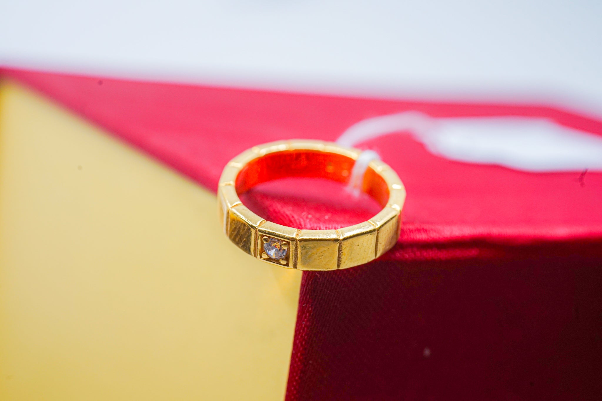 22k gold geometric band ring with square segments and a single clear stone accent, photographed on a red and yellow box.