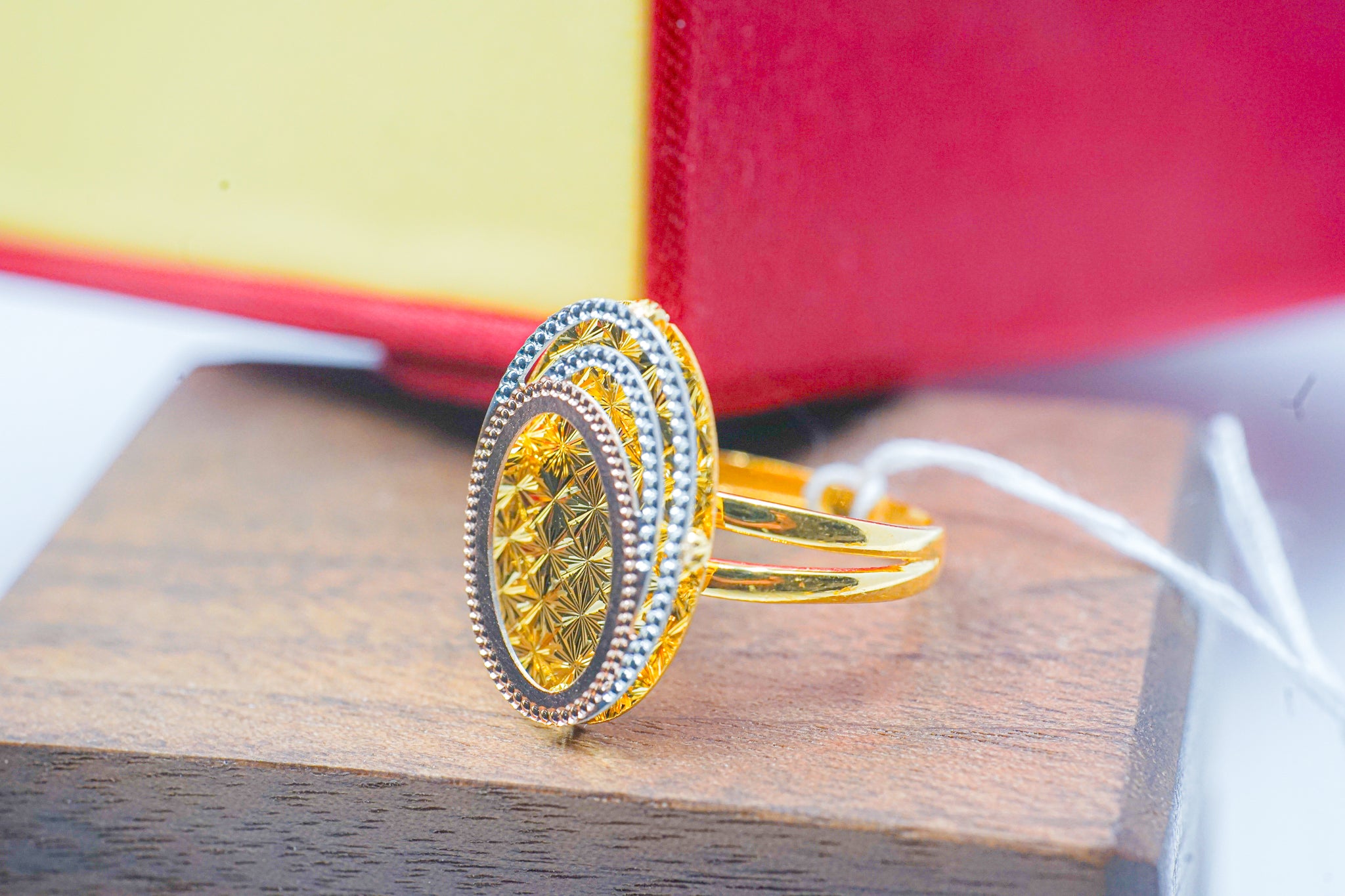 22k gold oval ring with textured geometric face and tri-tone border on wooden display.