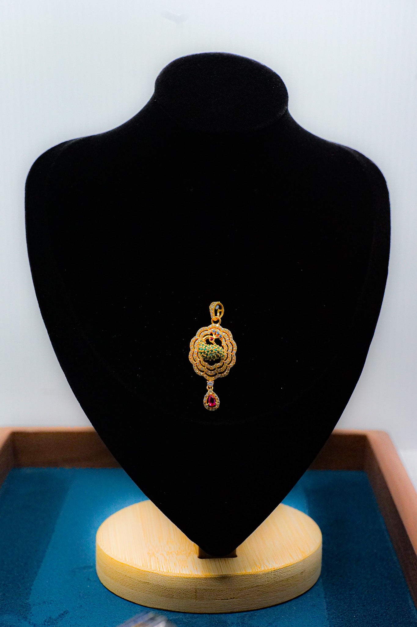 22k gold pendant with green detail and red teardrop dangle on a black jewelry display bust.