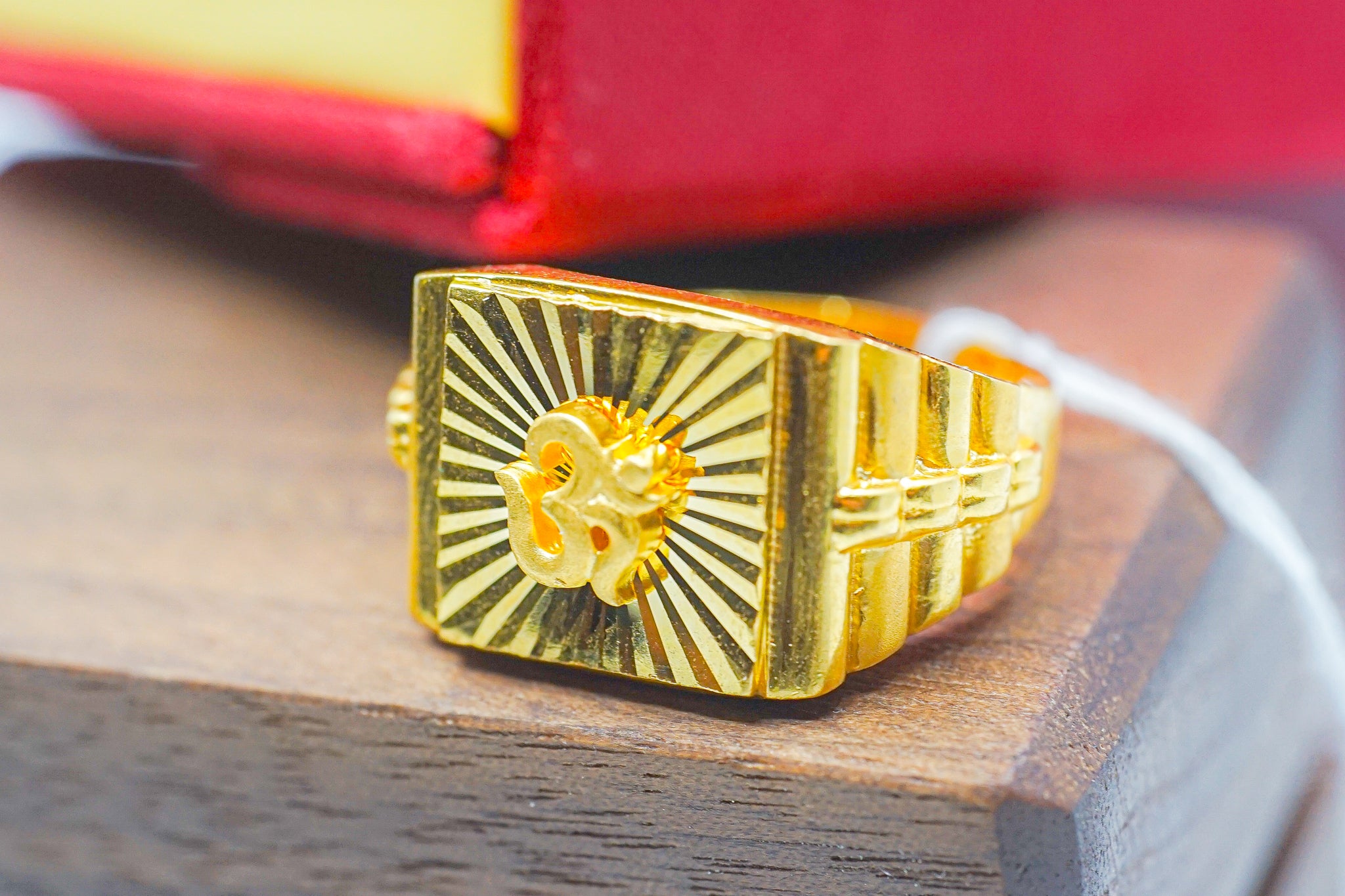 22k gold signet ring (7.42g) with square sunburst face, photographed on a wooden surface.