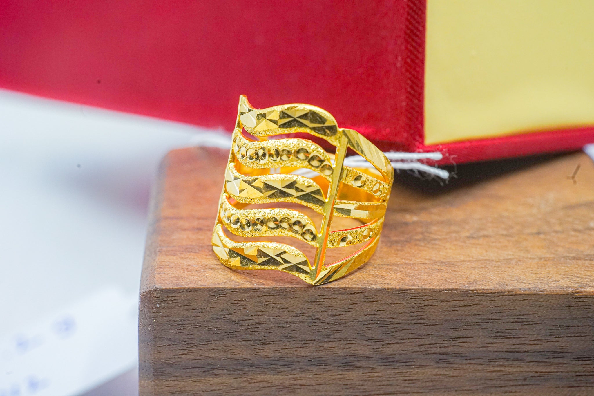 22k gold wide band ring with geometric wave cutout and textured finish, shown on a wooden block.