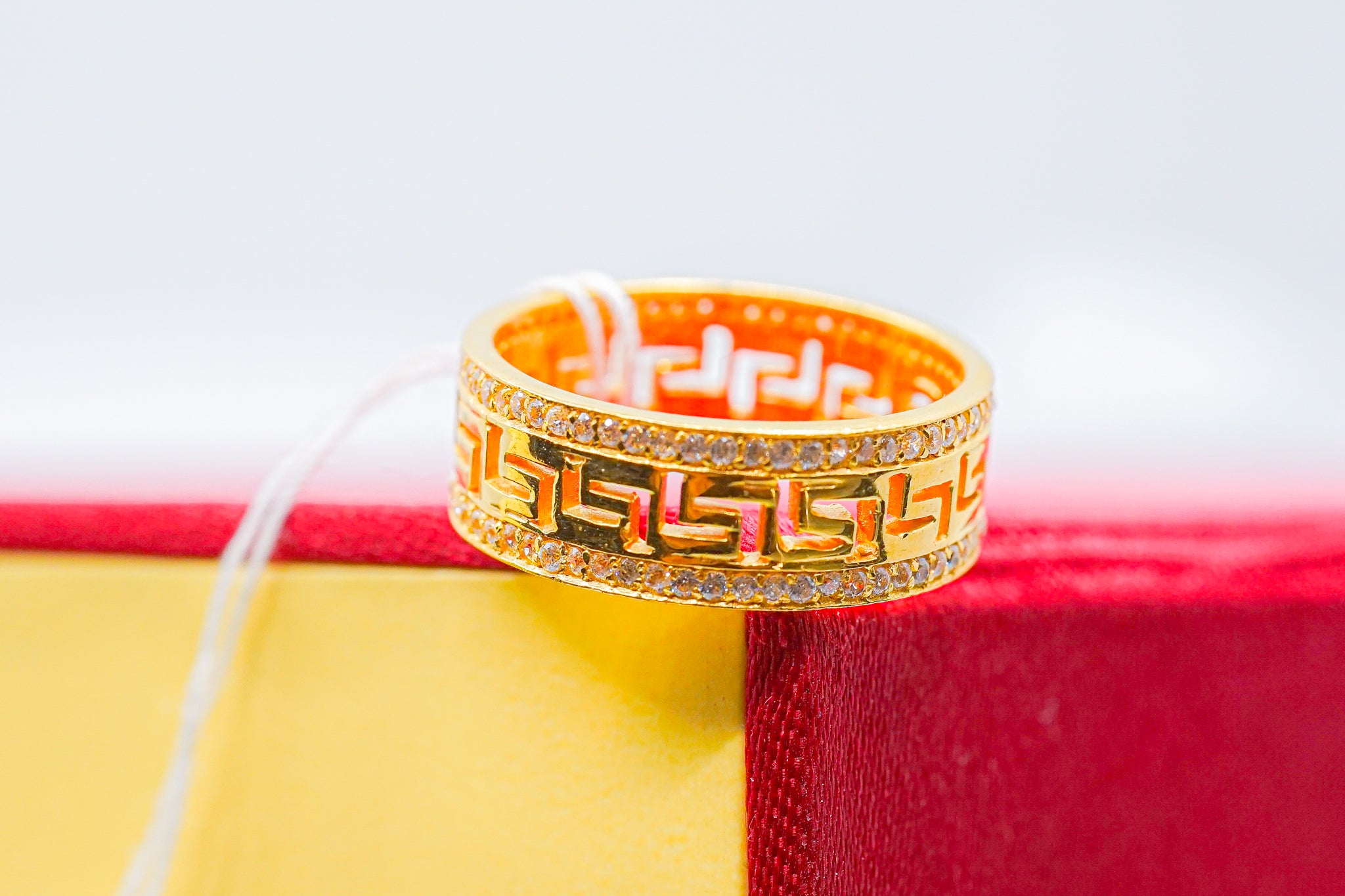 22k gold wide band ring with Greek key geometric design and clear accent edges, shown on red and yellow box