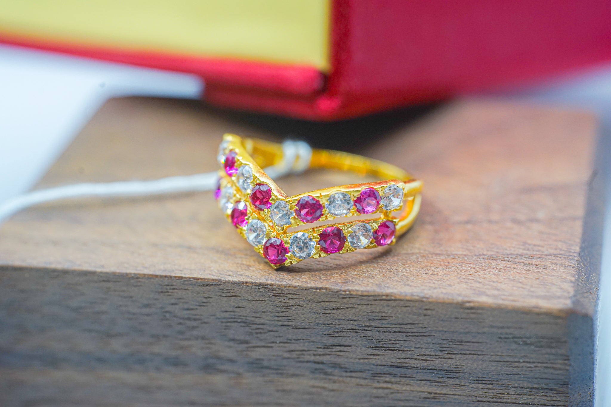 22k gold zirconia ring with pink and white stones on a wooden display