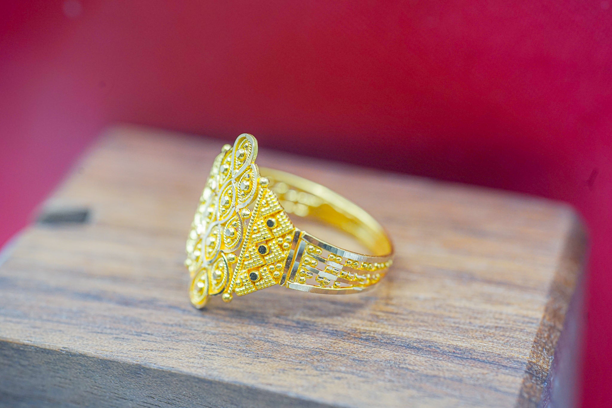 22k solid gold filigree statement ring on a wooden display with red background