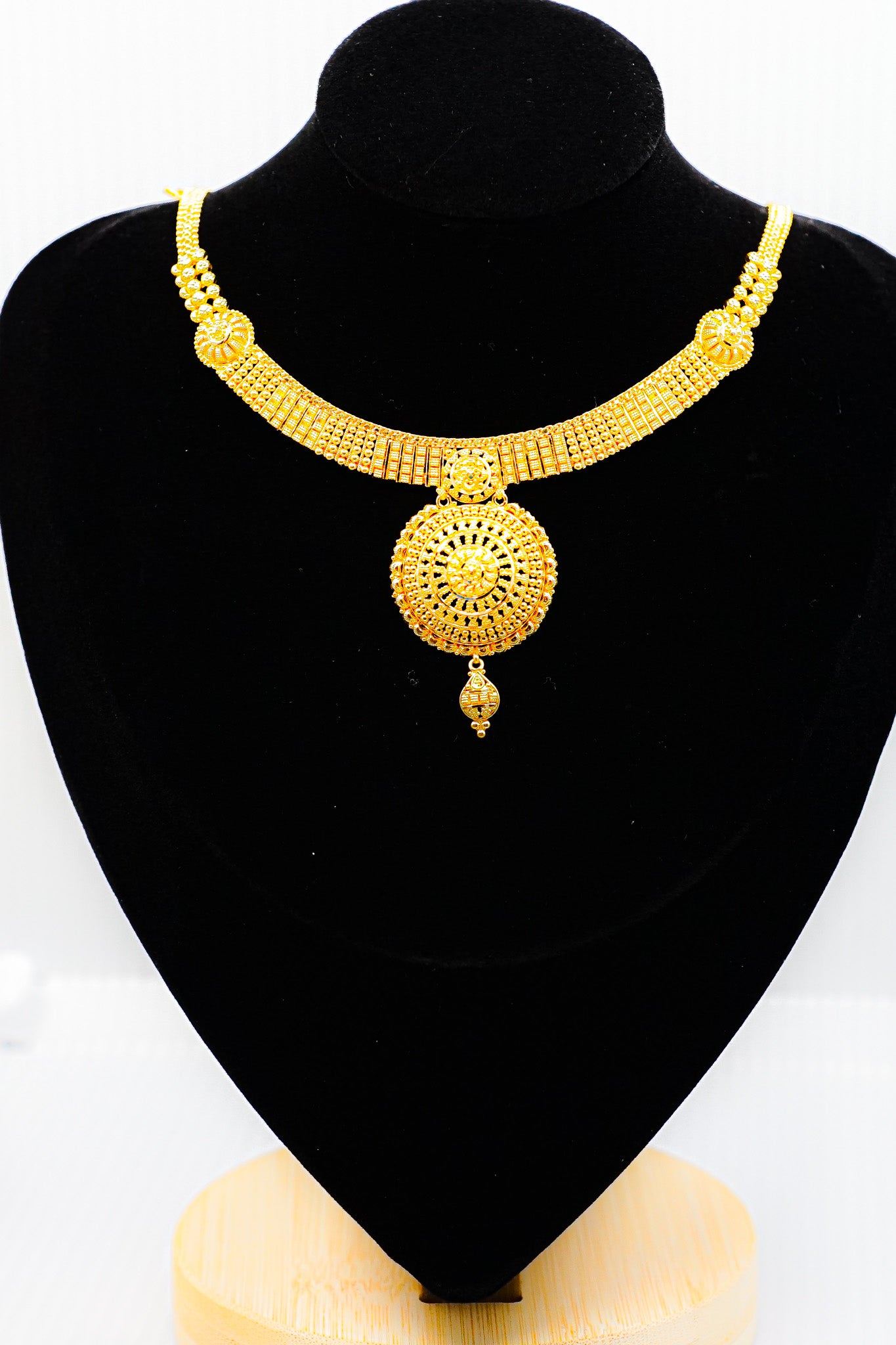 22k yellow gold collar necklace with round pendant on a black mannequin bust