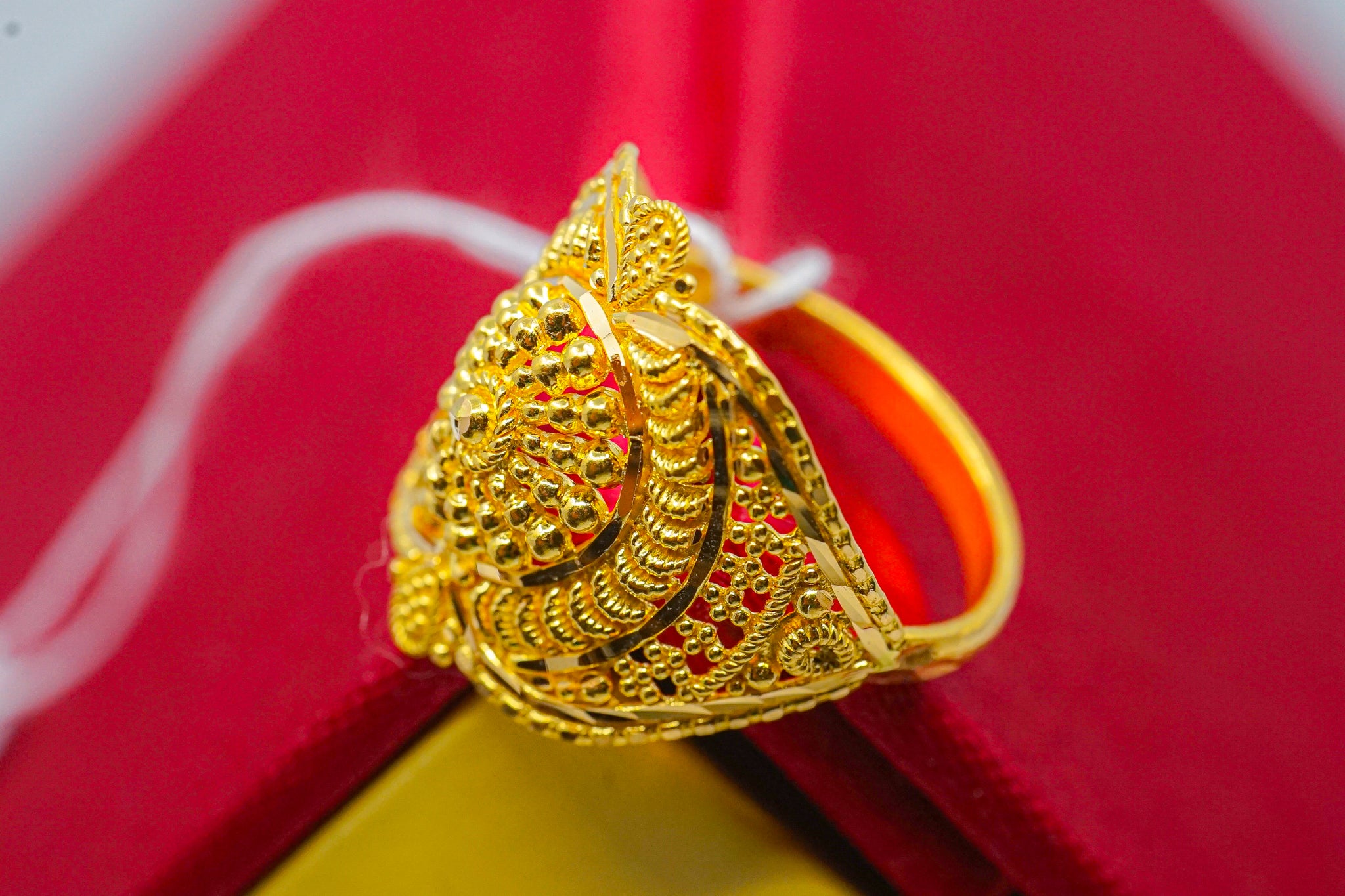 22k yellow gold filigree statement ring with triangular face, photographed on a red jewelry box