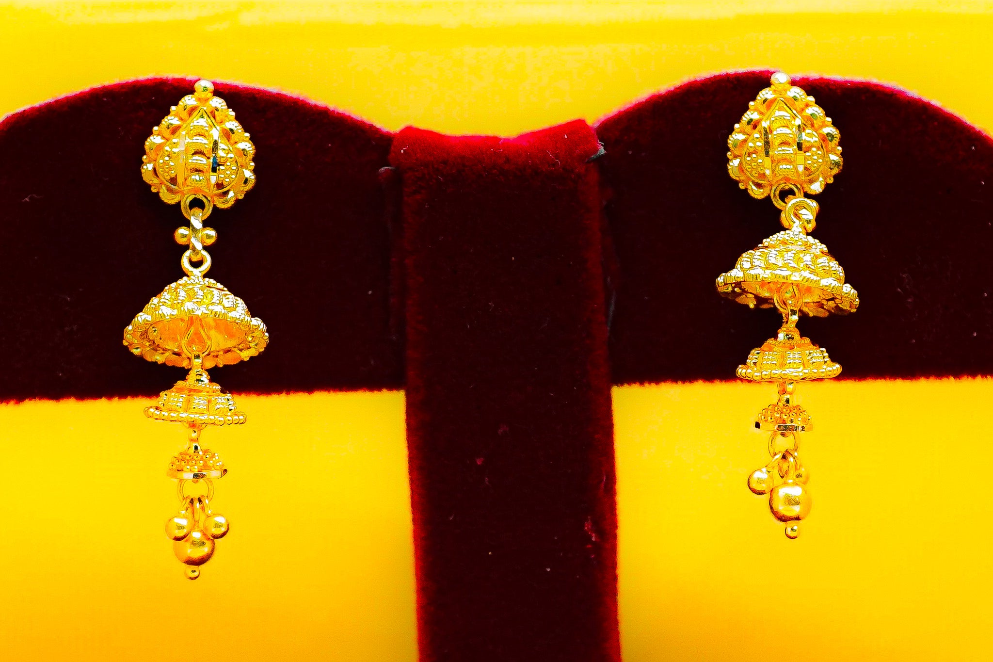 22k yellow gold jhumka drop earrings displayed on a red velvet stand
