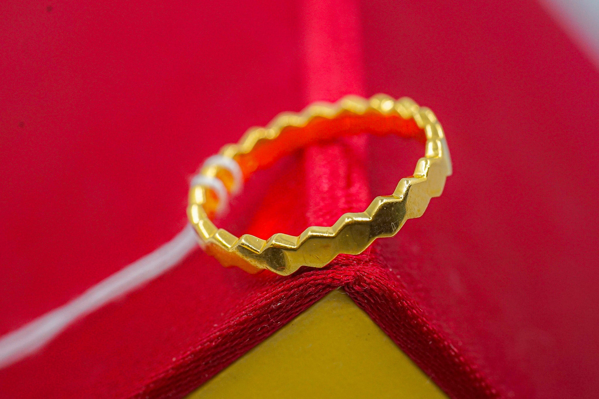 22k yellow gold zigzag edge band ring, 2.69g, close-up on red and yellow background