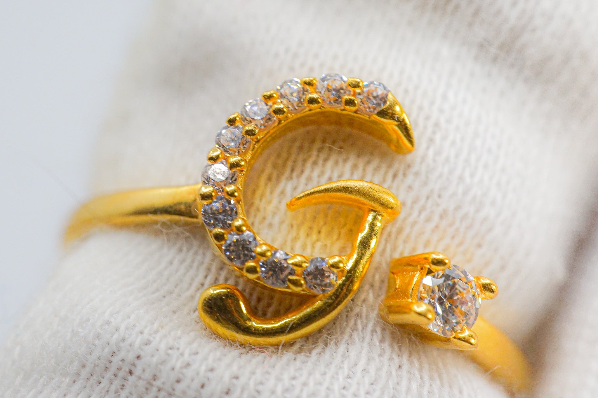 22k gold letter G ring with clear stones, shown close-up on a fabric background