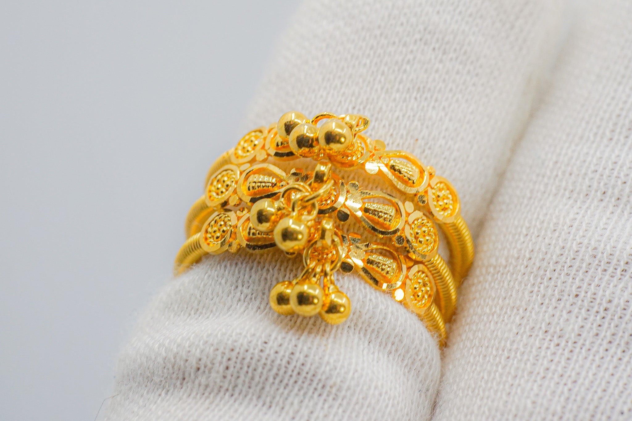 Angle view of a 22k yellow gold beaded ring with dangling bead charms