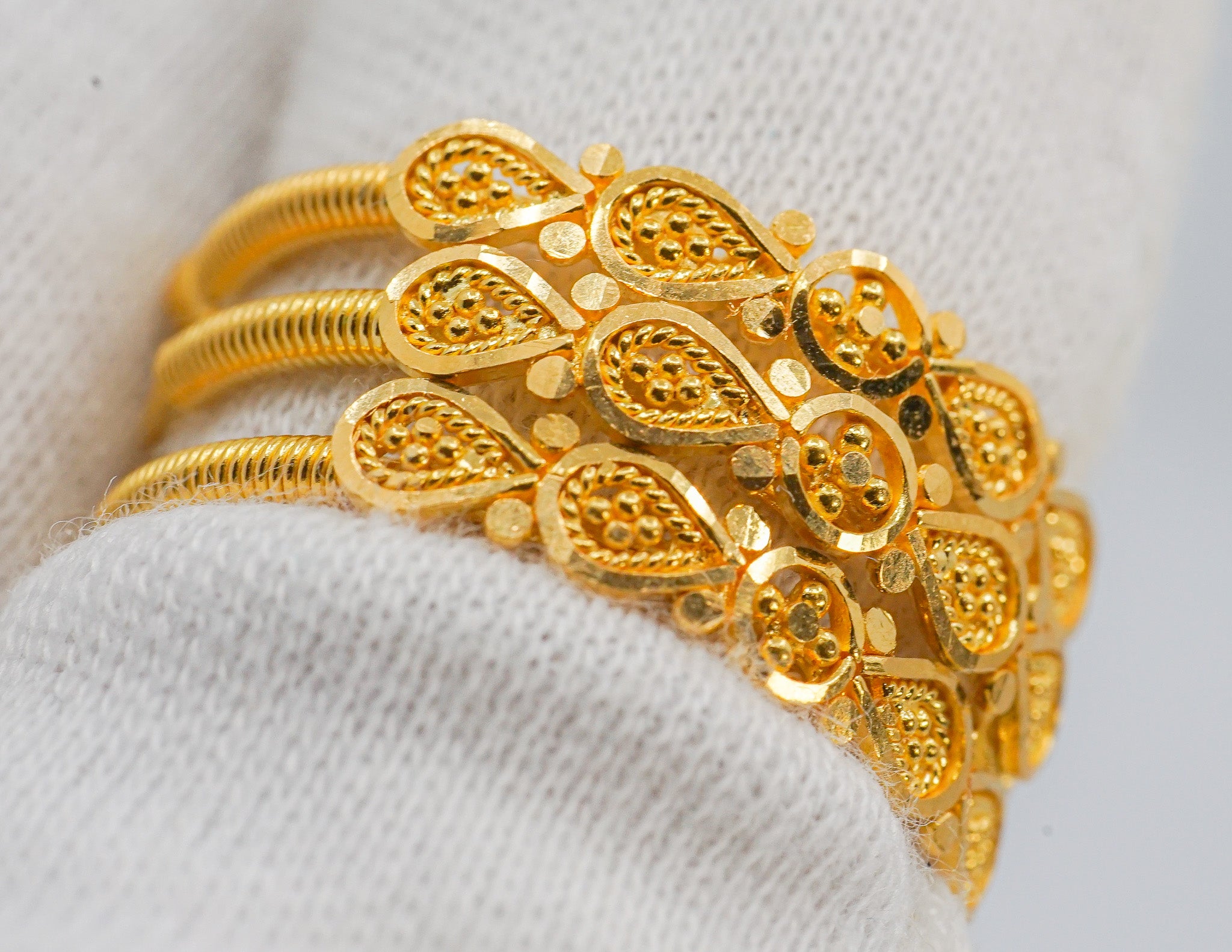 Angled view of 22k gold wide band ring with teardrop pattern and multi-row coil shank