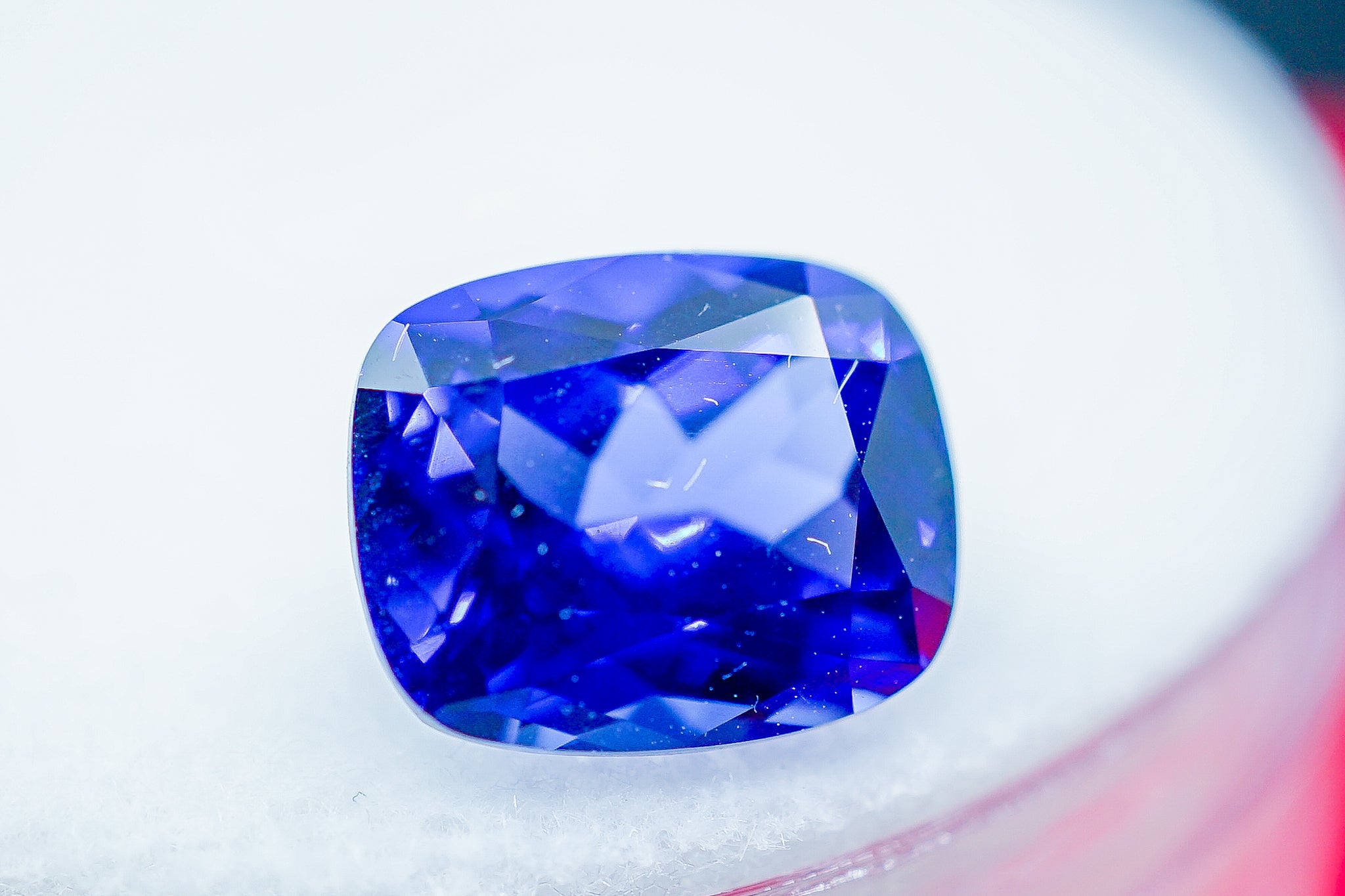 Blue sapphire cushion cut gemstone held with tweezers on white background