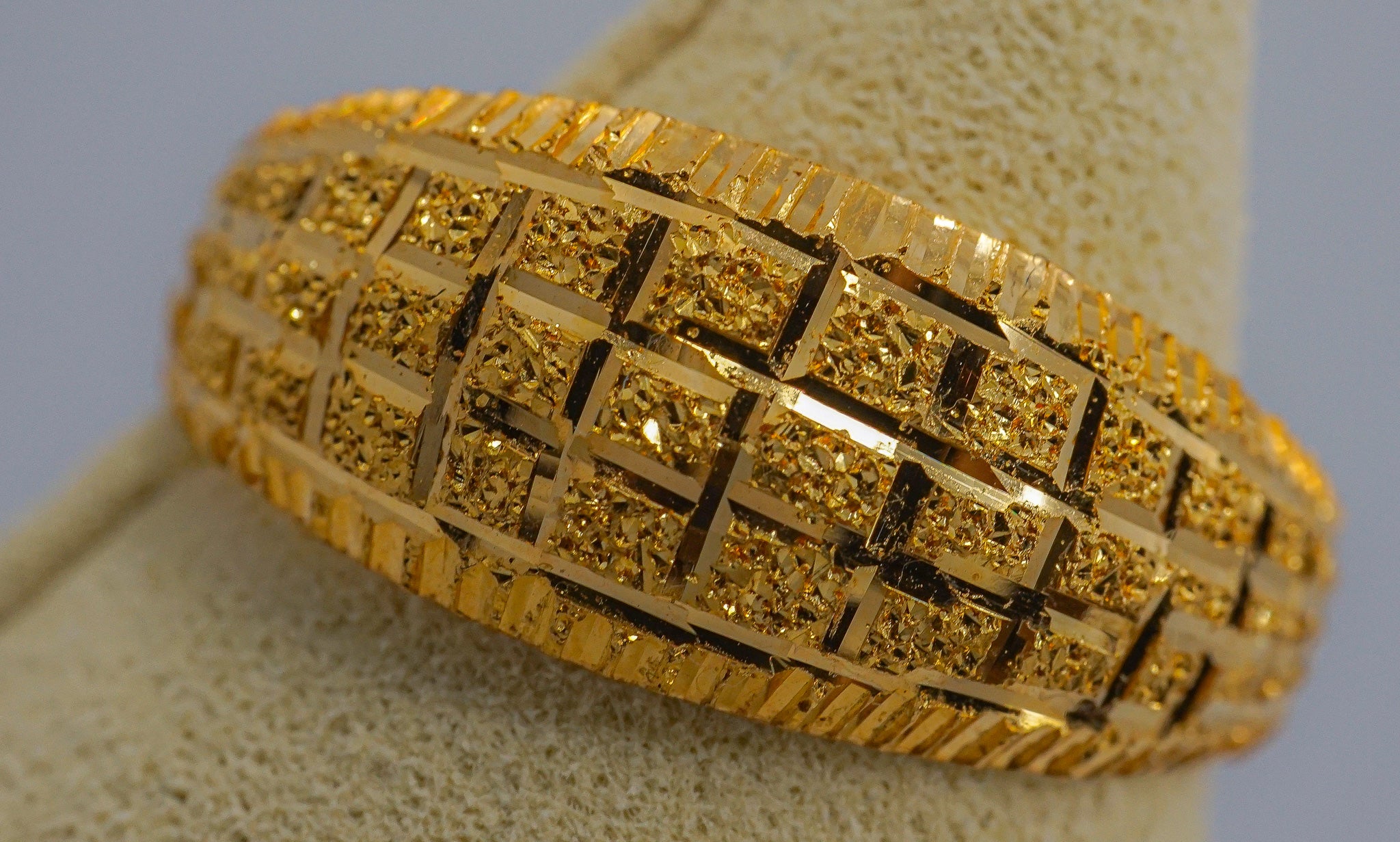 Close-up of a 22K gold wide band ring with a geometric textured grid pattern