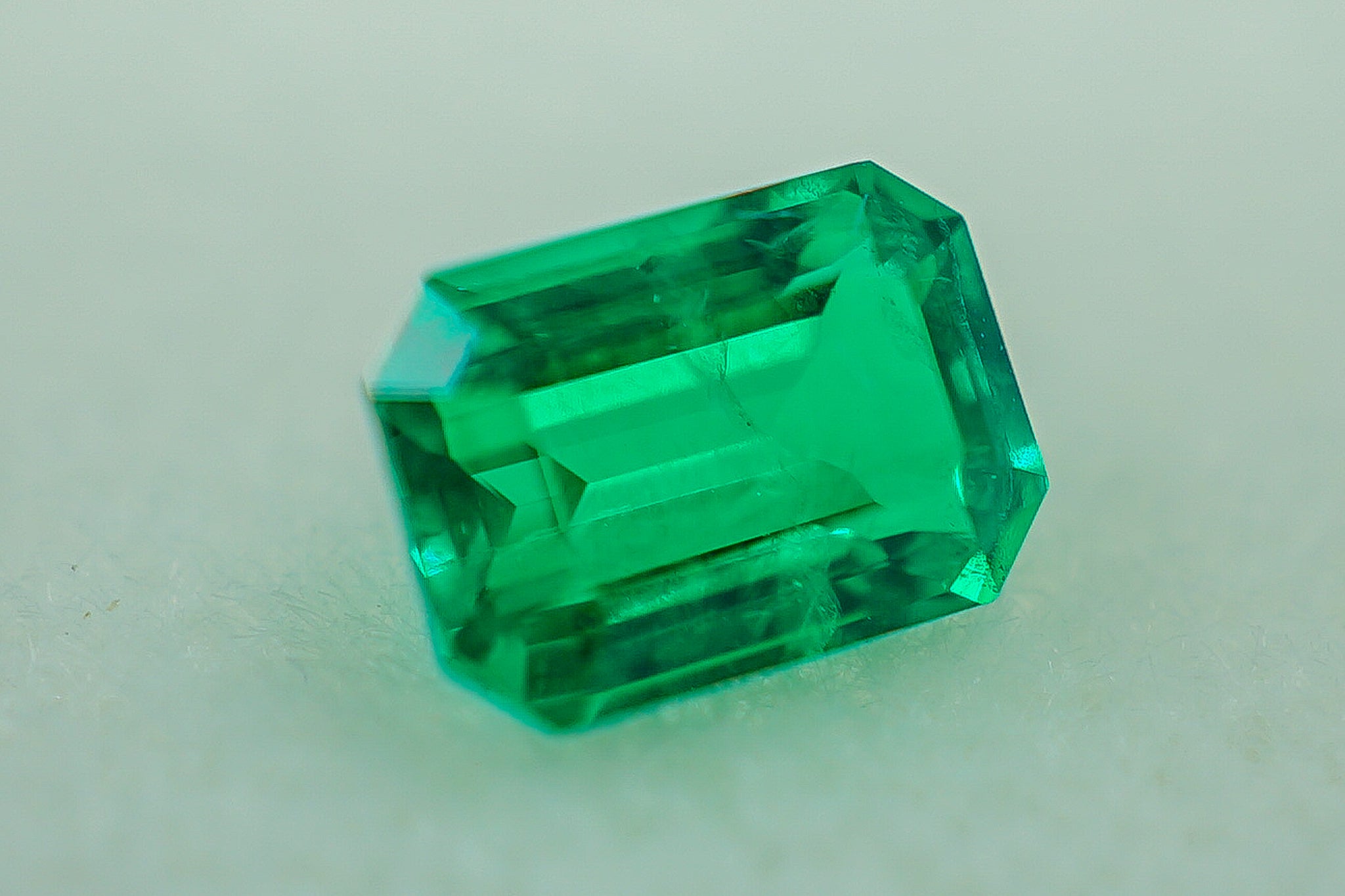 Close-up of green emerald gemstone 0.17 g in rectangular emerald cut on light gray background