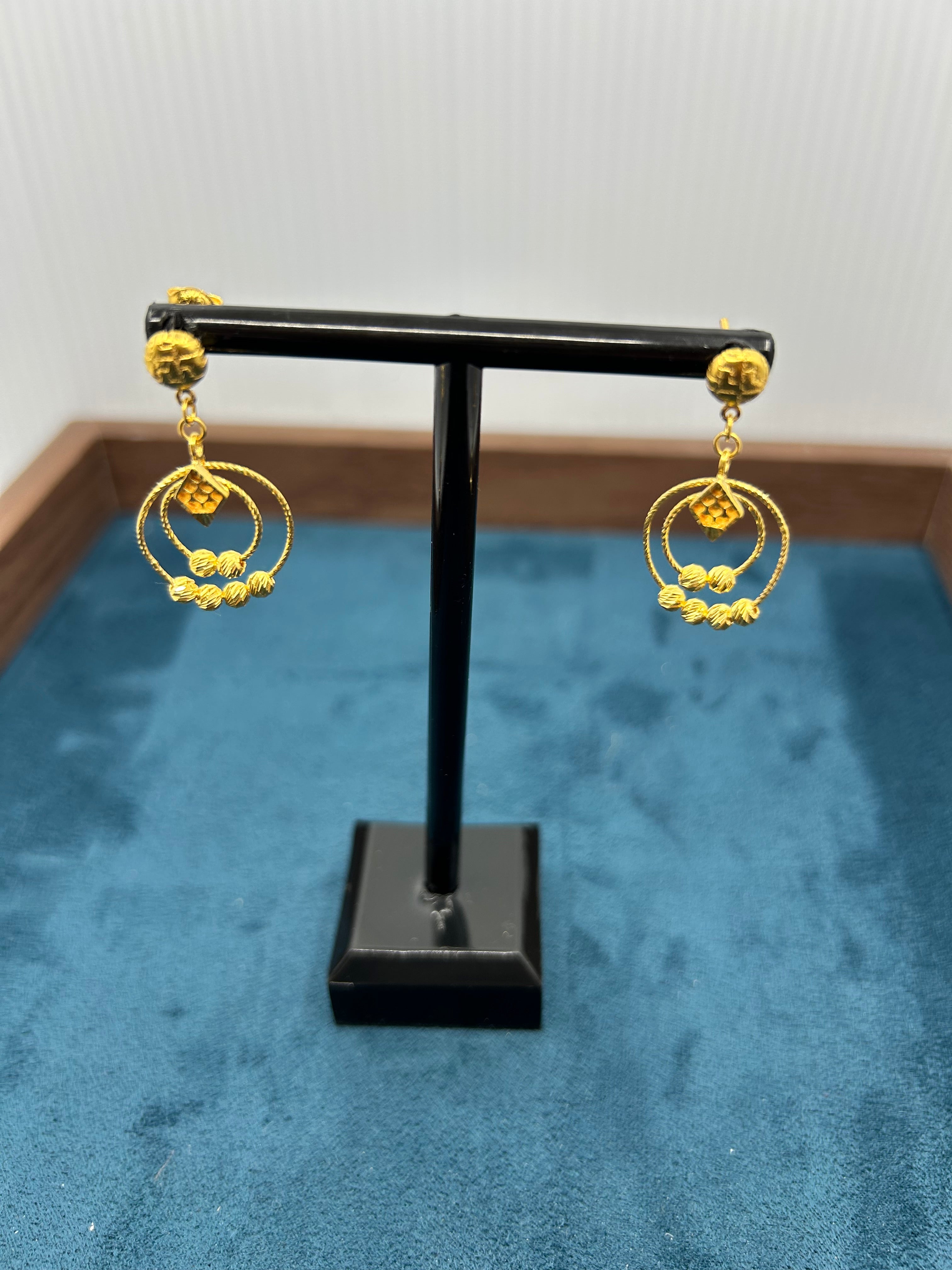 Gold earrings on a black stand against a blue textured background