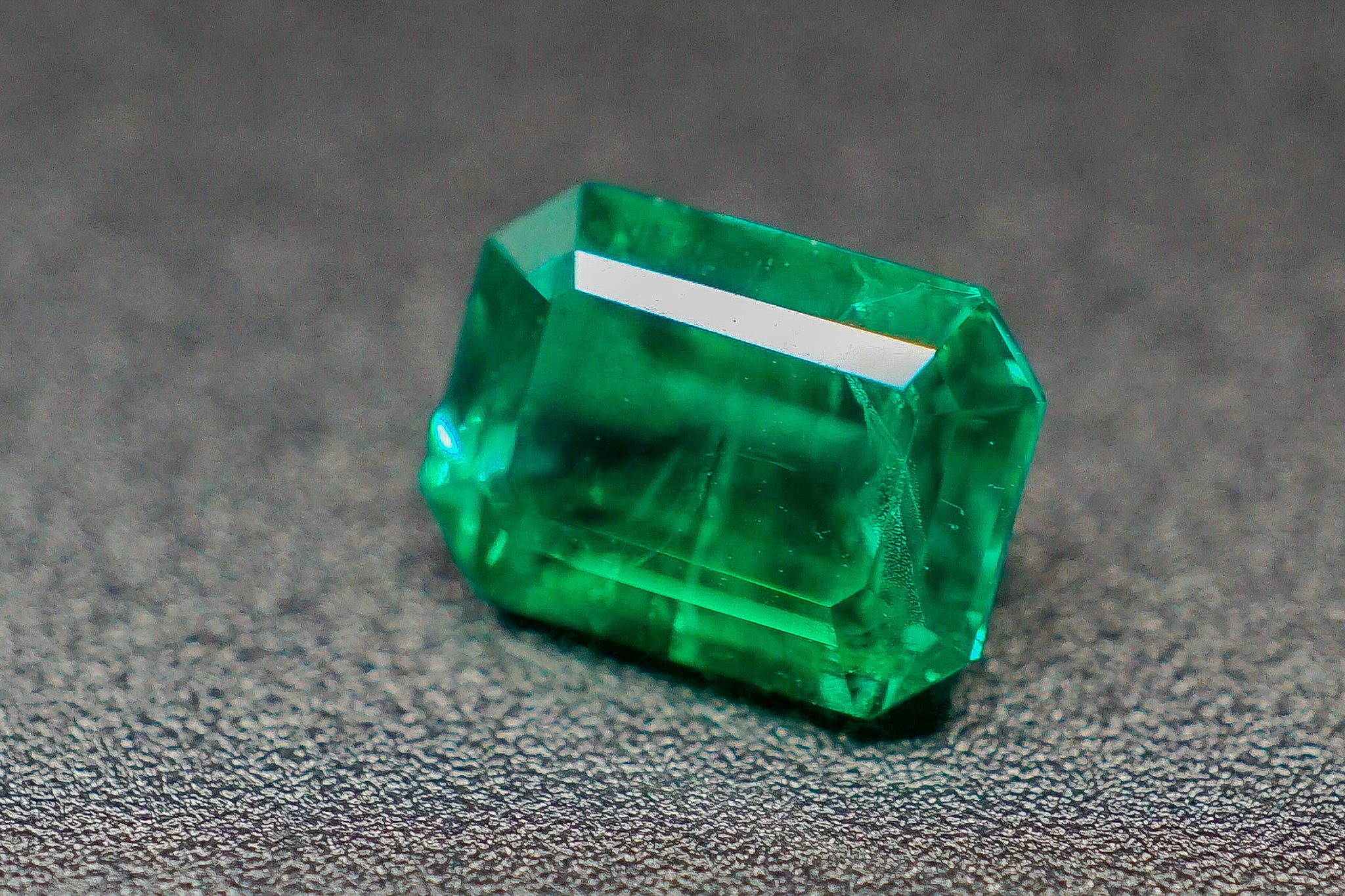 Emerald-cut loose emerald stone 0.28g rectangular green gemstone on gray surface