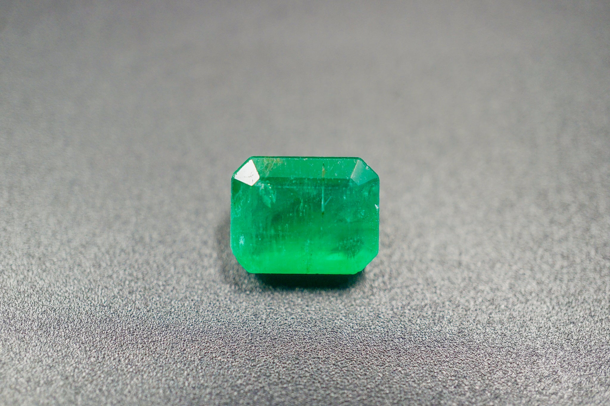 Emerald cut green emerald stone on a gray textured background (0.63 g)