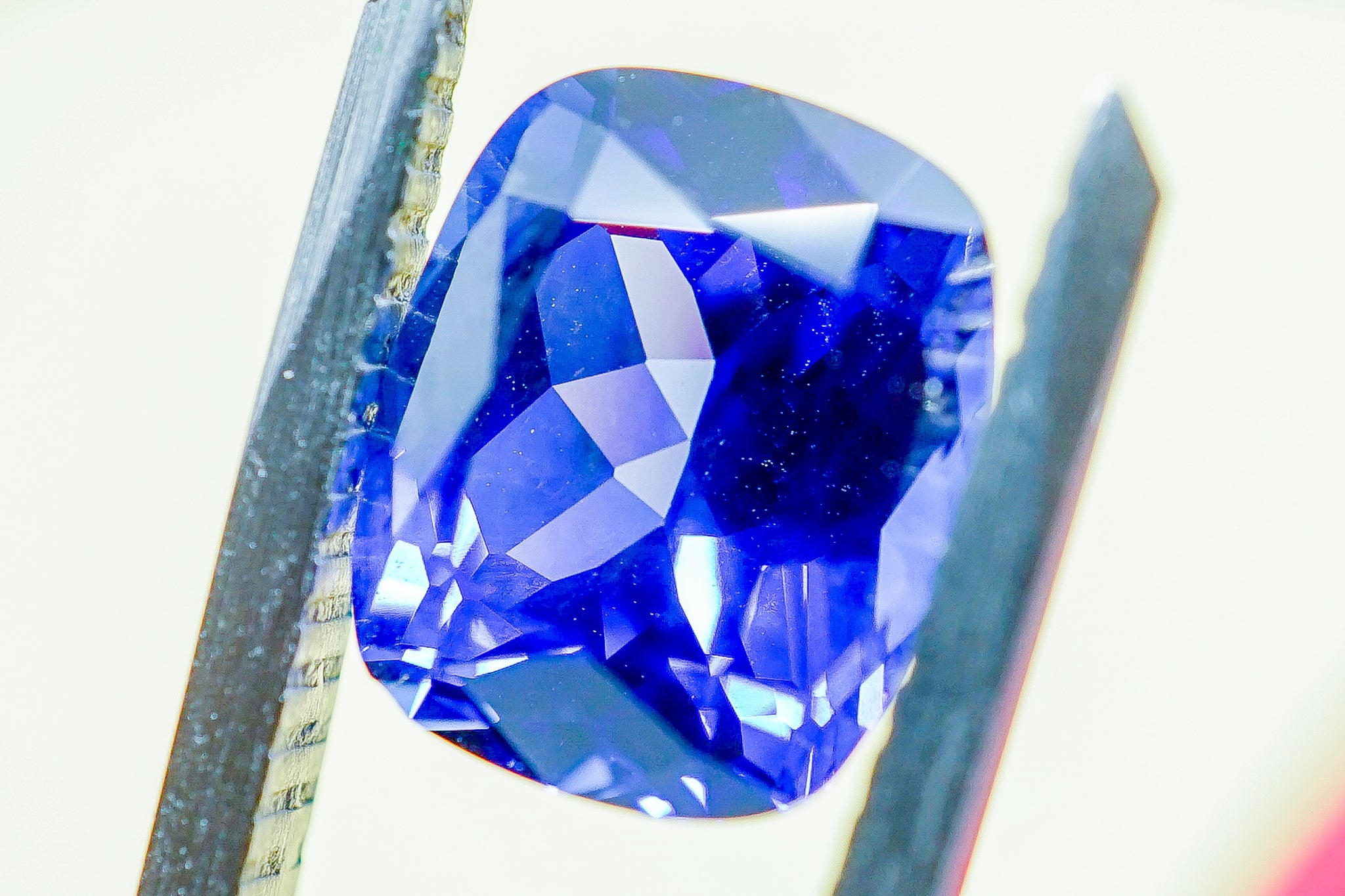 Faceted oval blue sapphire gemstone held with tweezers