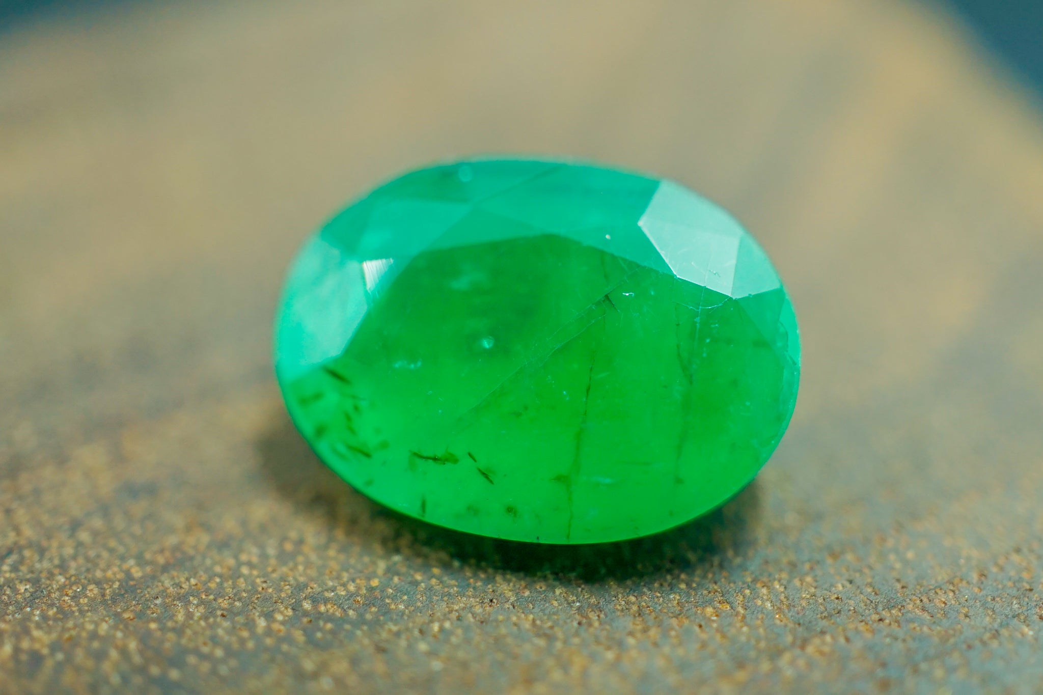  Faceted oval green emerald stone close-up on textured surface